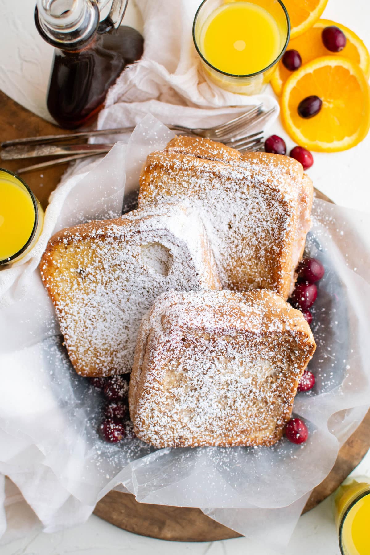 white napkin, powdered sugar covere french toast sandwiches, cranberries, orange slices, orange juice