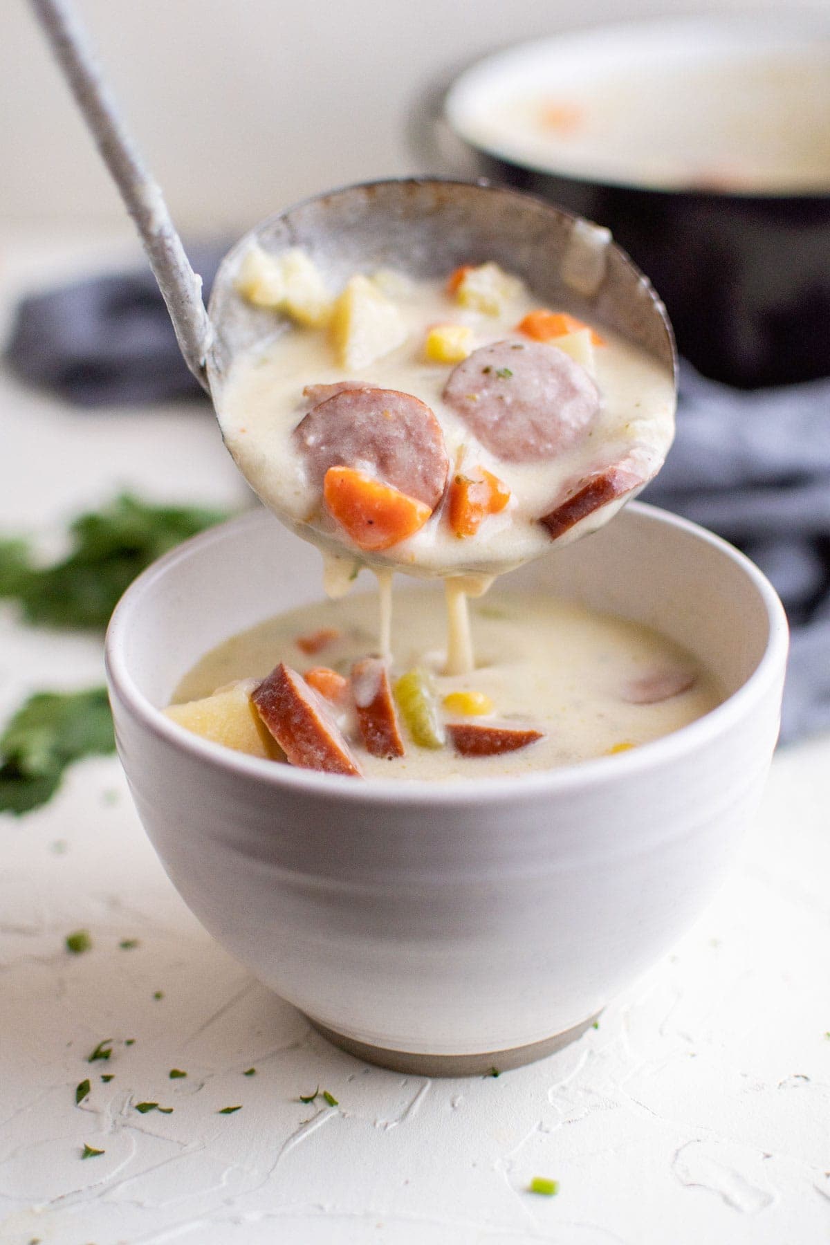 white bowls, ladle pouring sausage and potato soup