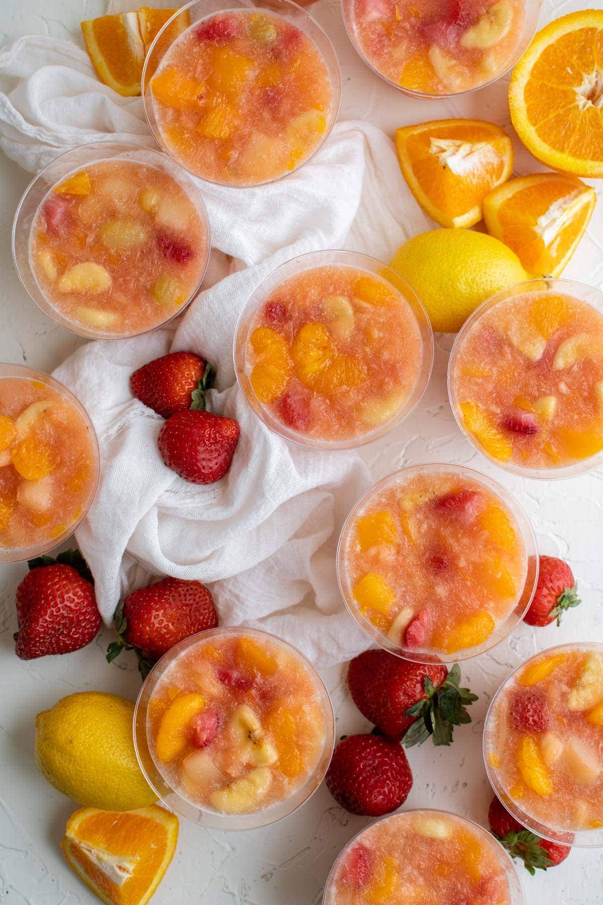 clear plastic cups with frozen fruit, strawberries, oranges, white towel.