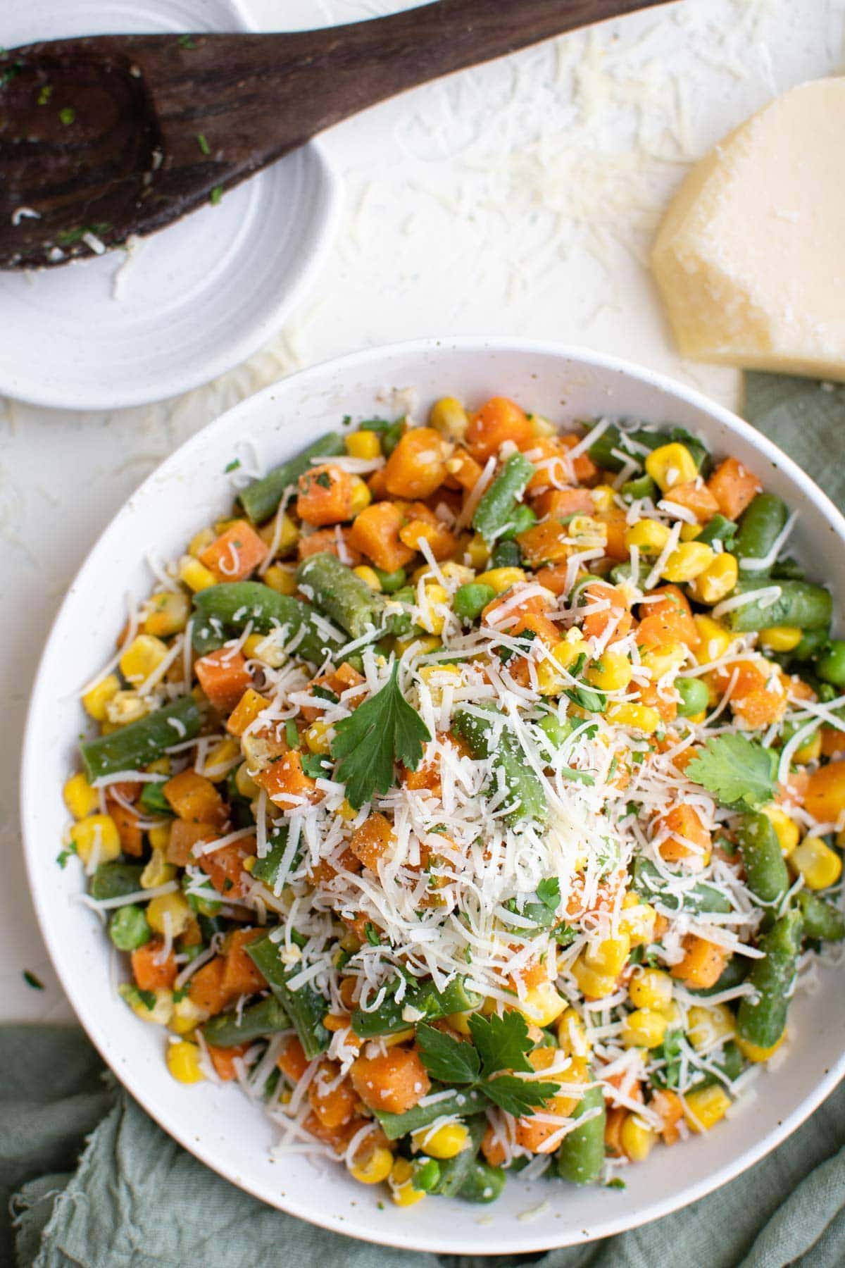 white plate, frozen vegetables, cooked, parmesan cheese, wood spoon