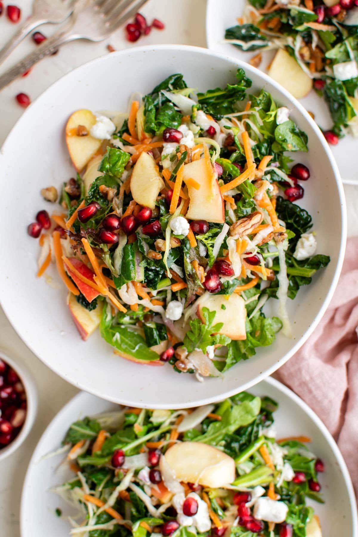 white plates with salad on them, forks, pomegranate seeds