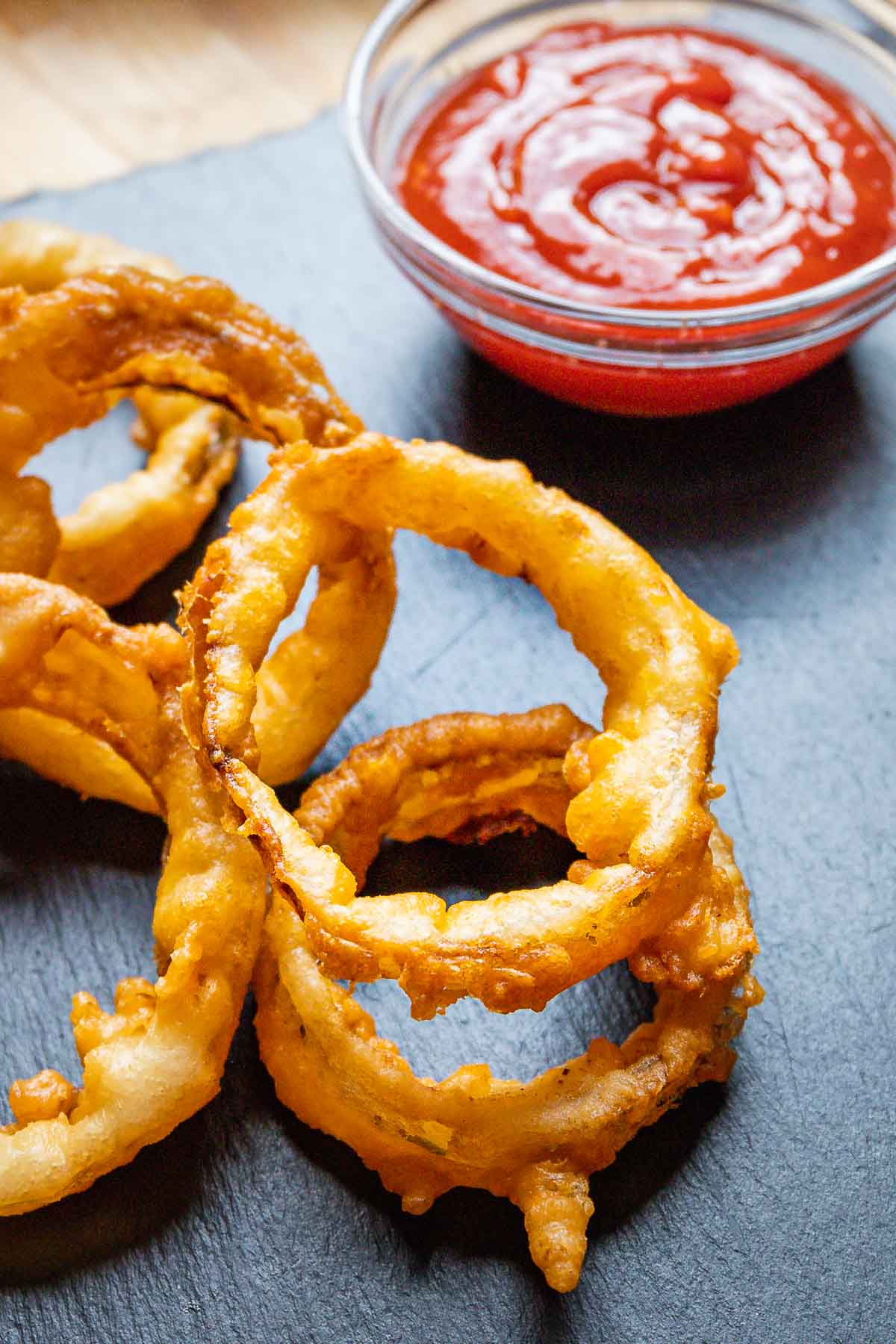 Onion rings and ketchup bowl on black slate board.