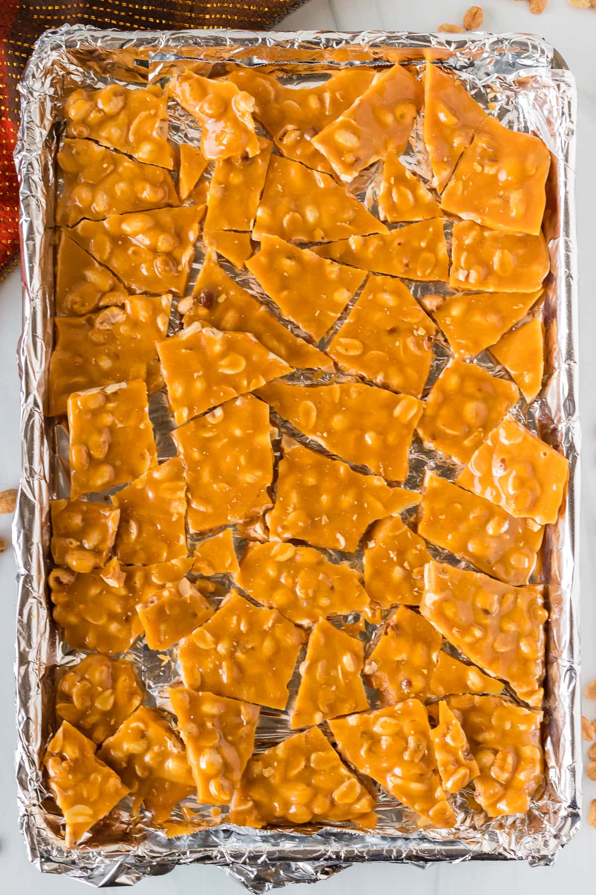 overhead shot of baking sheet with broken pieces of peanut brittle