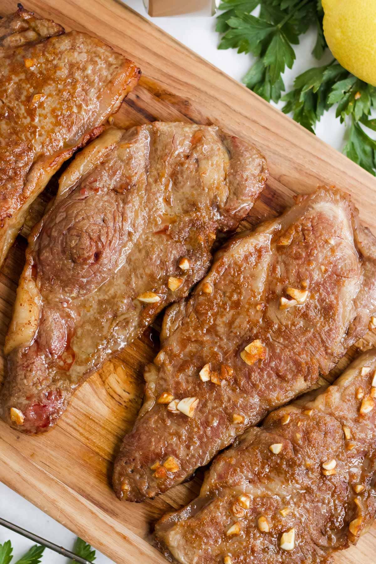 new york strip steaks cooked, cutting board, parsley, lemon