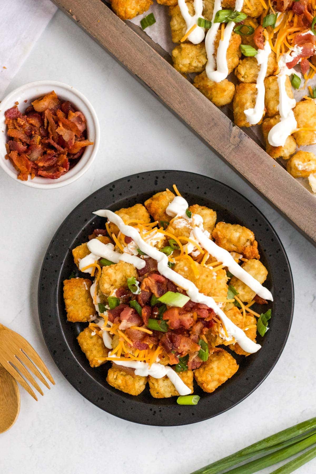 tater tot nachos with sour cream, bacon, green onions and cheese, black plate, wood tray