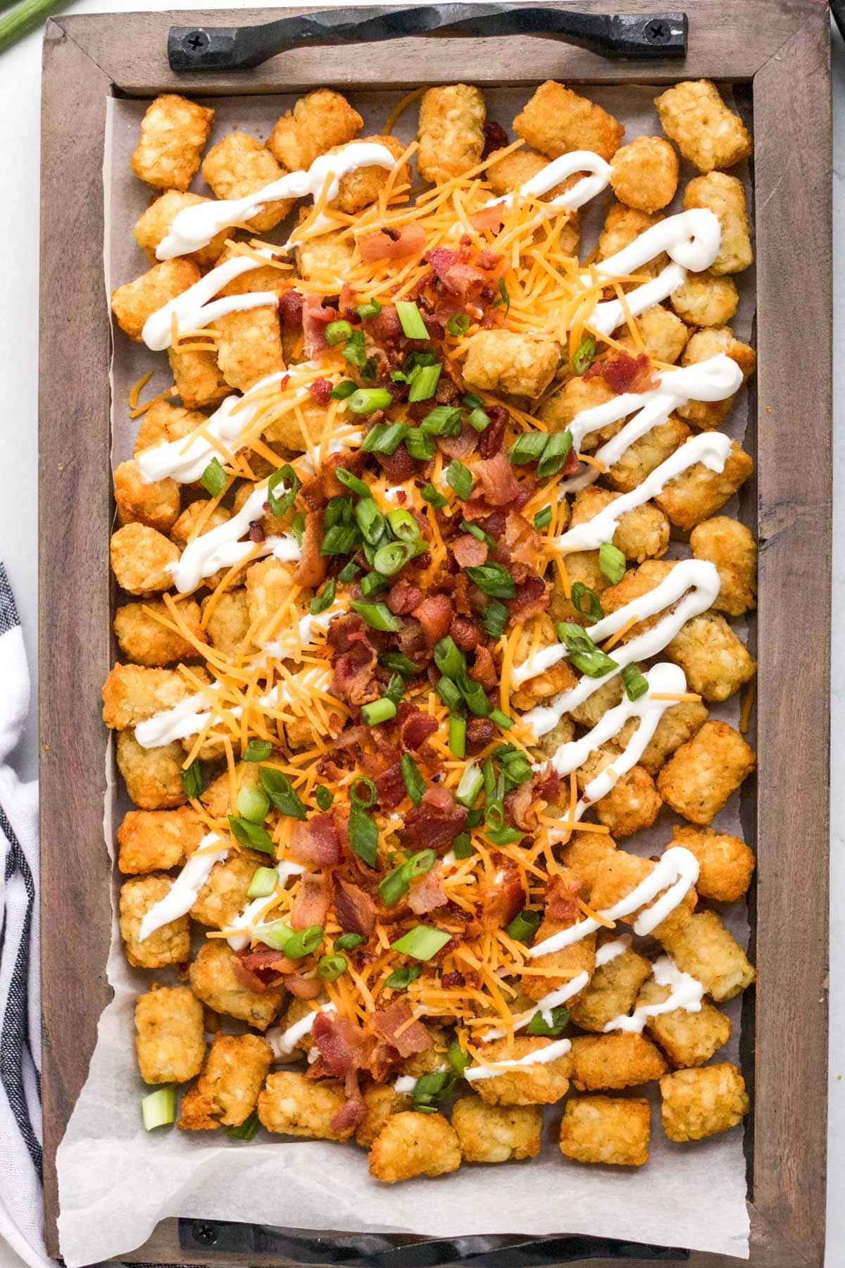 tray of tater tots with cheese, sour cream, green onions and bacon