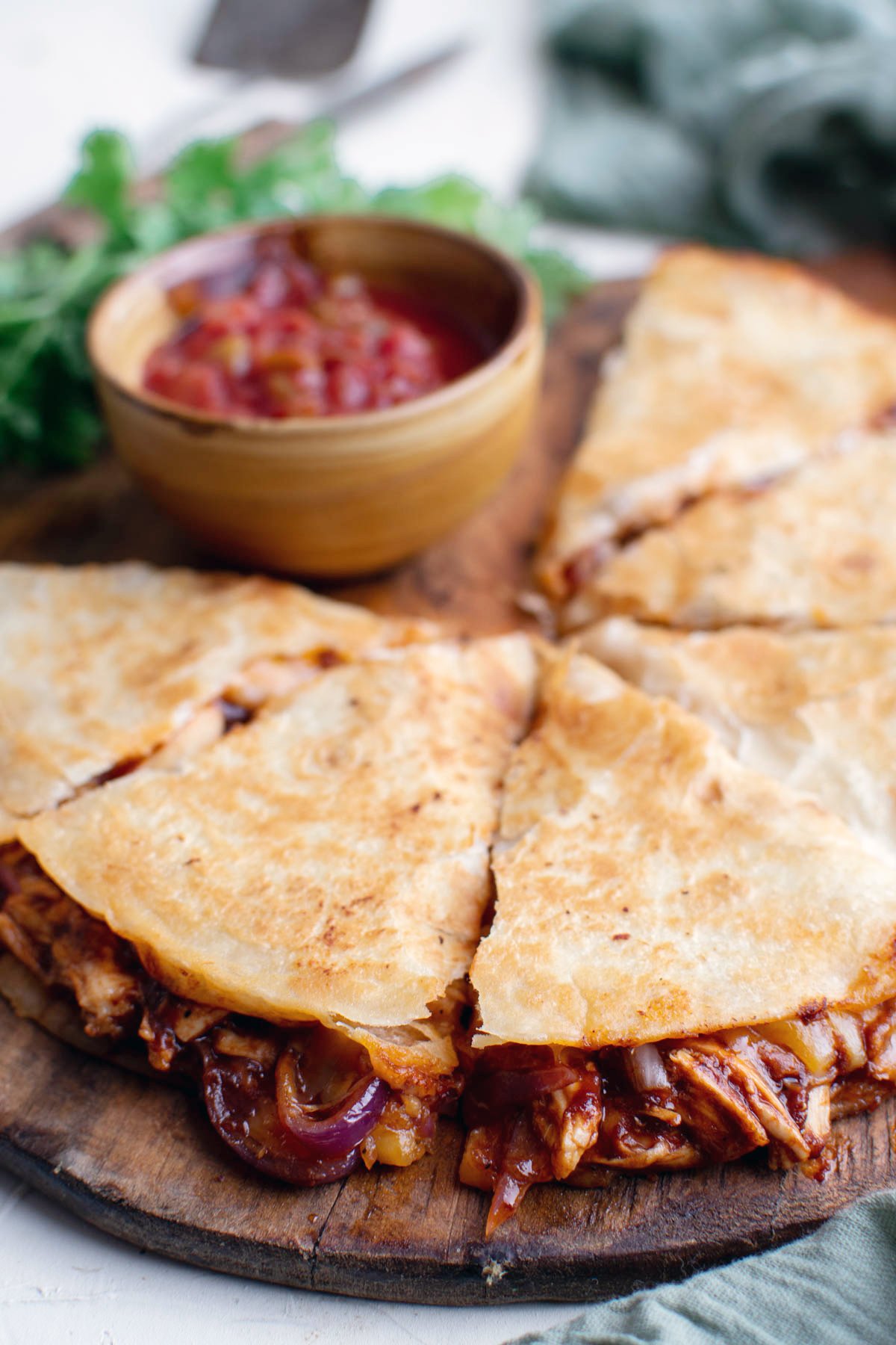 sliced bbq chicken quesadilla with dish of salsa on wood cutting board