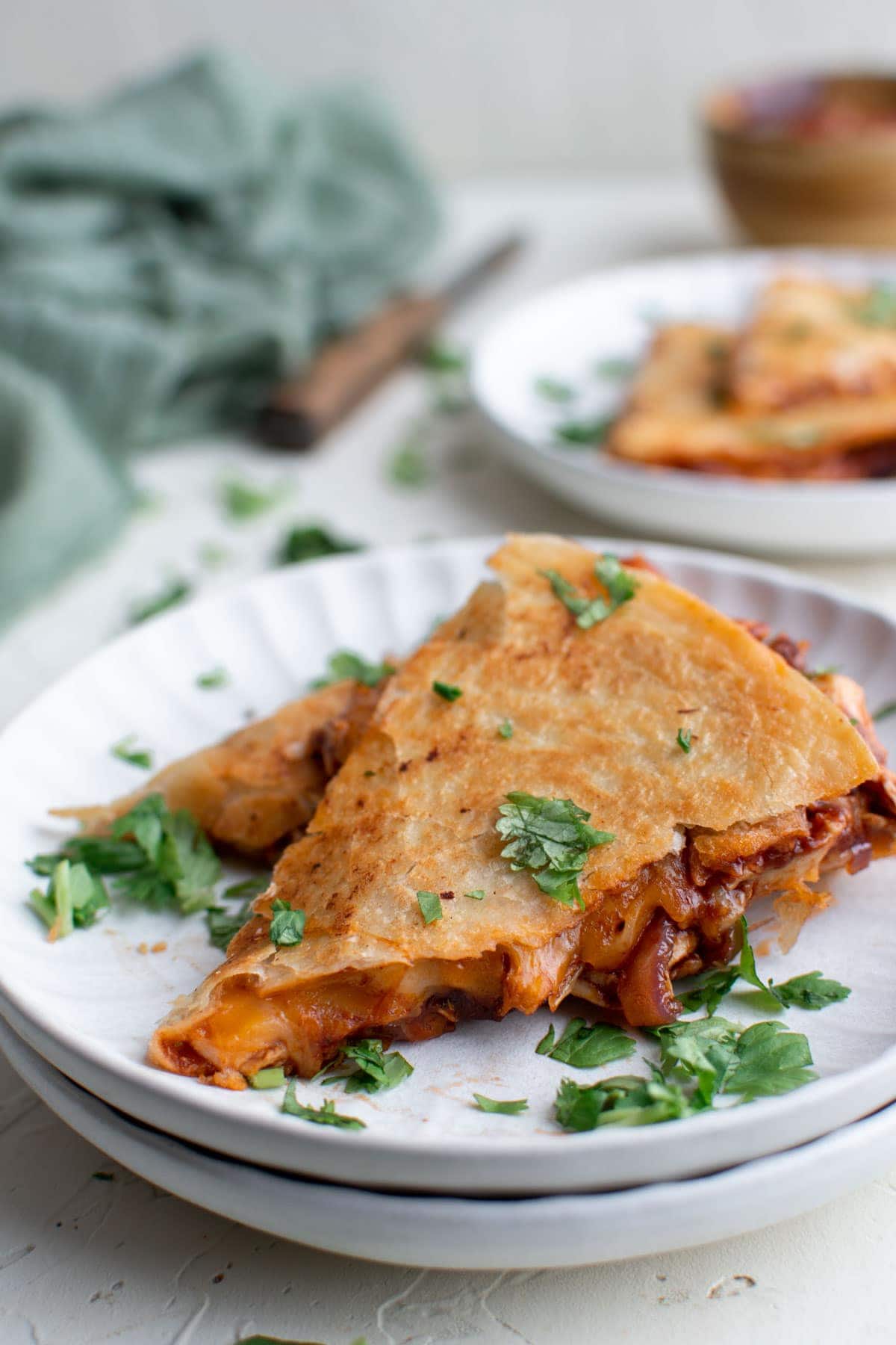 slices of chicken quesadilla on white plates, a green napkin, cilantro