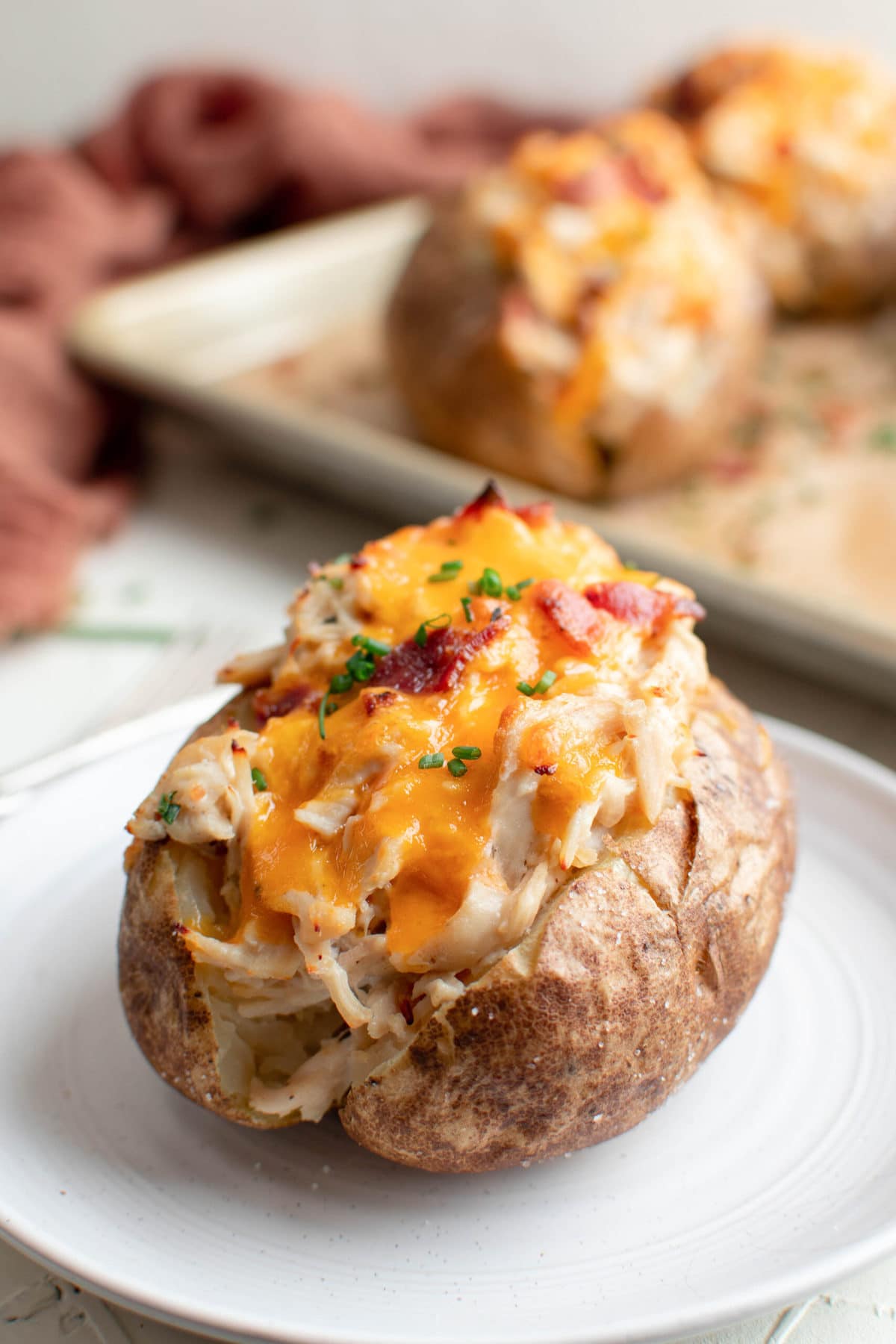 backed potato stuffed with crack chicken, melted cheese and bacon, white plate, baking sheet