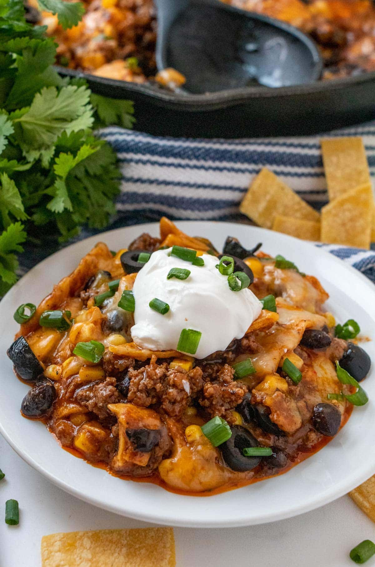 white bowl, skillet enchiladas, sour cream, olives, green onions, cheese, ground beef, cast iron skillet ,tortilla strips