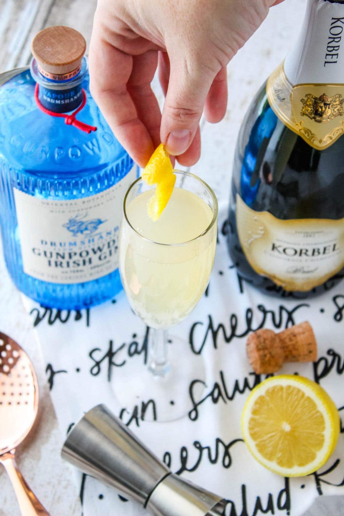 lemon curl being added to a cocktail in a champagne flute