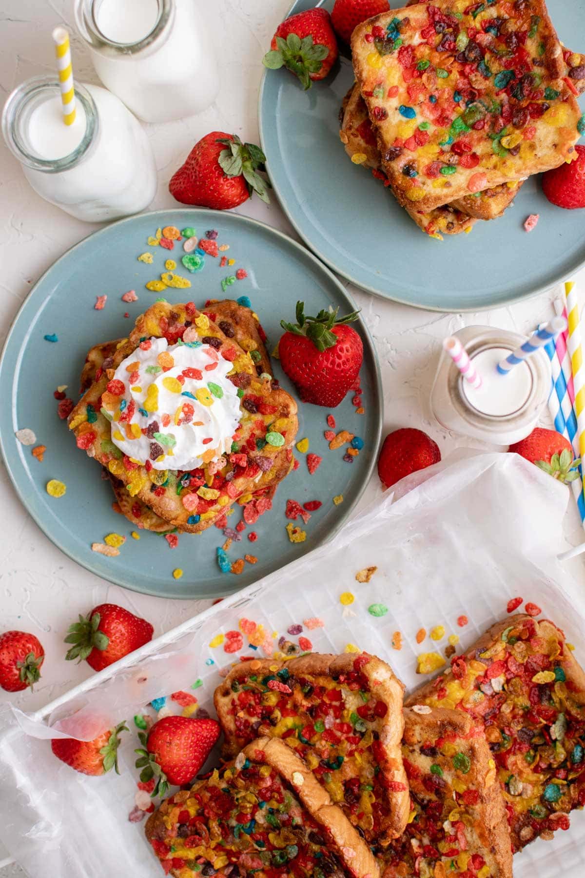 blue plates, glasses of milk, fruity pebbles, whipped cream, strawberries