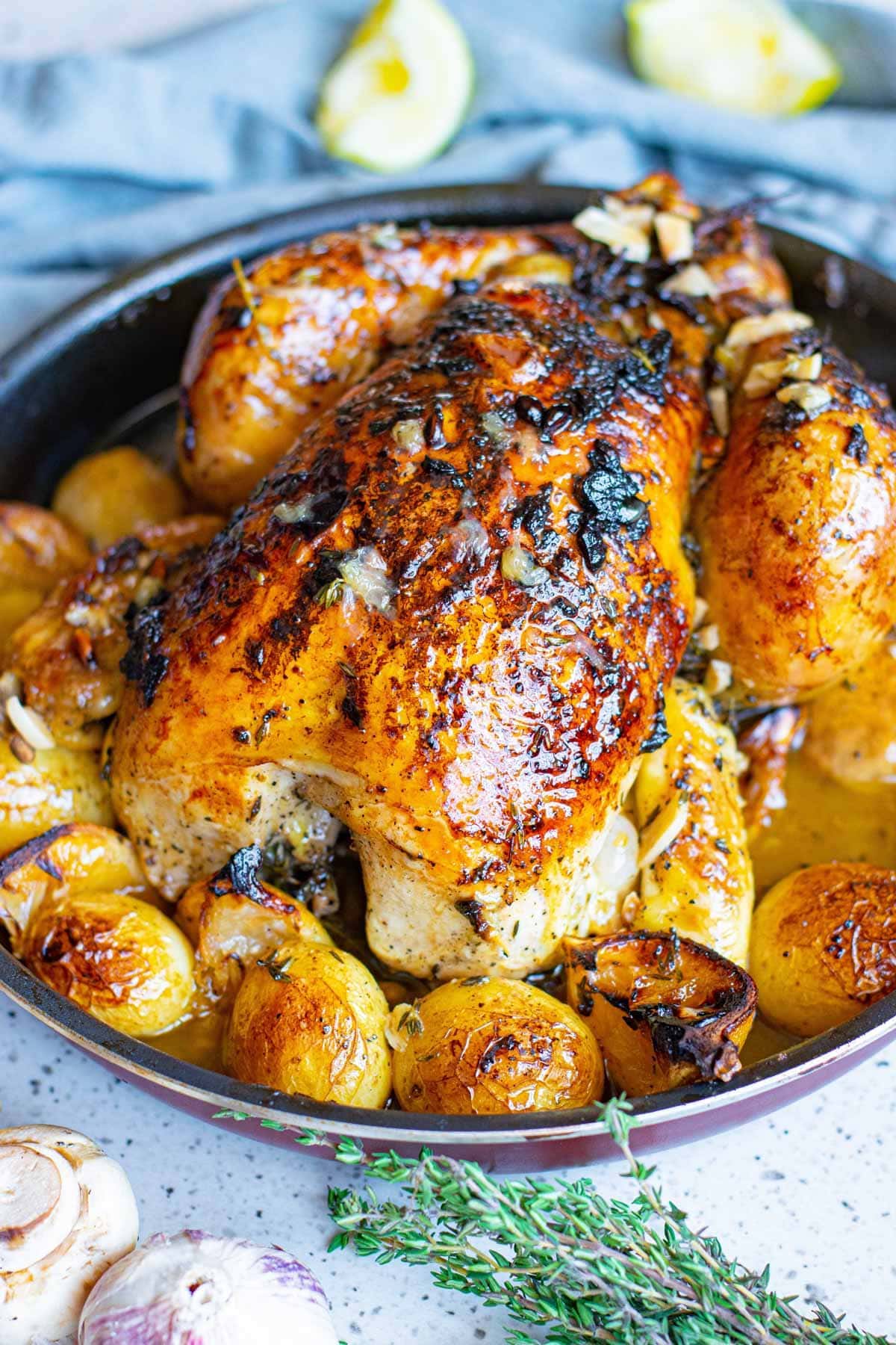 roast chicken in a round pan with potatoes and lemons, blue napkin