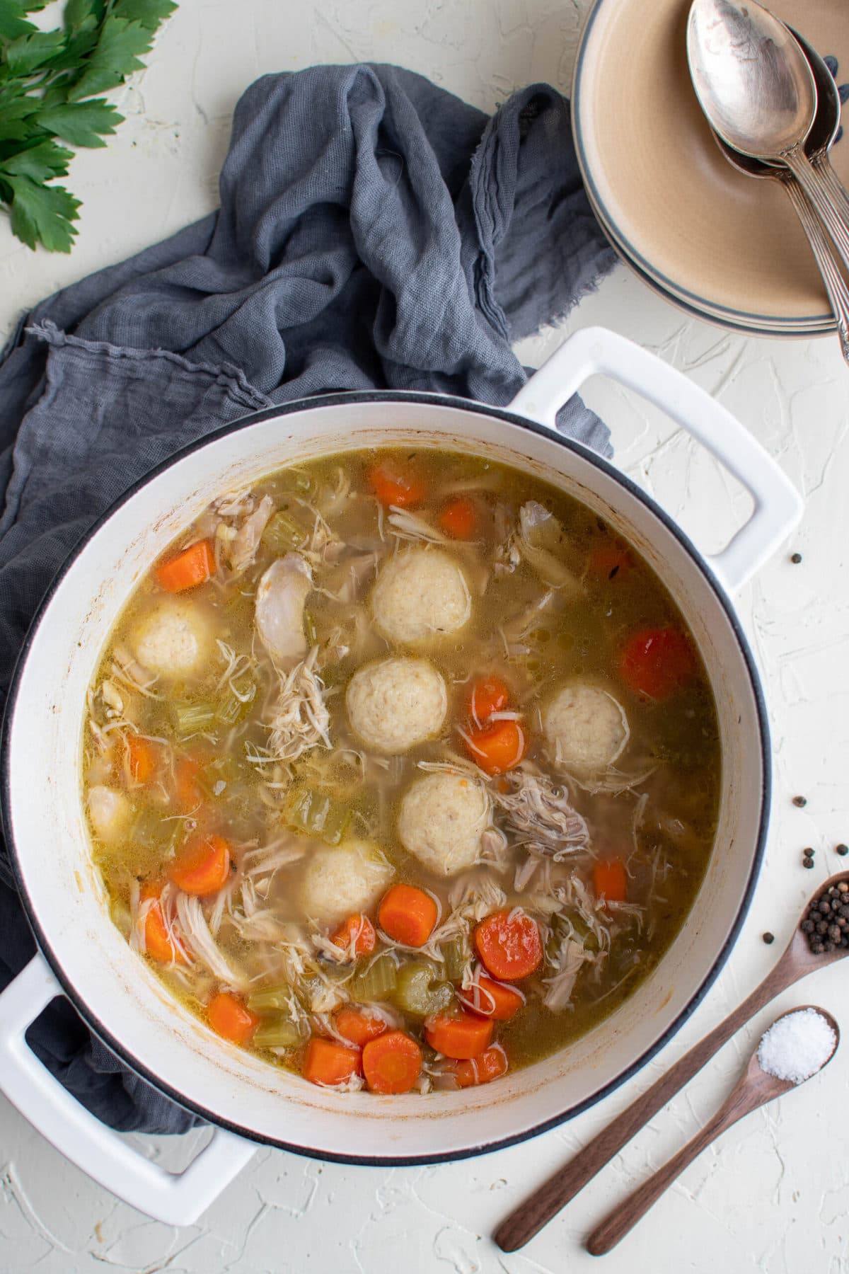 white soup pot, chicken sou and matzo balls, blue napkin, parsley