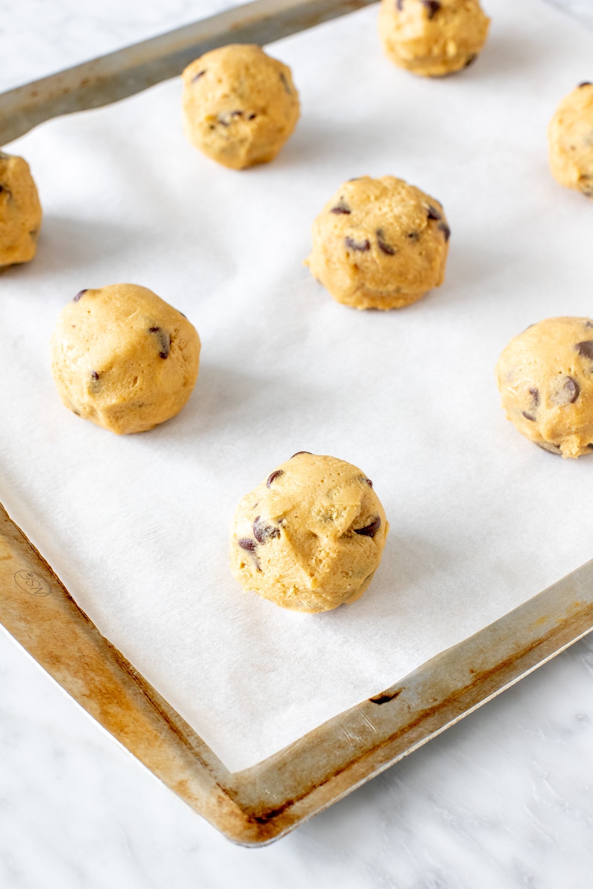 Chocolate chip cookie dough balls on a lined baking sheet.