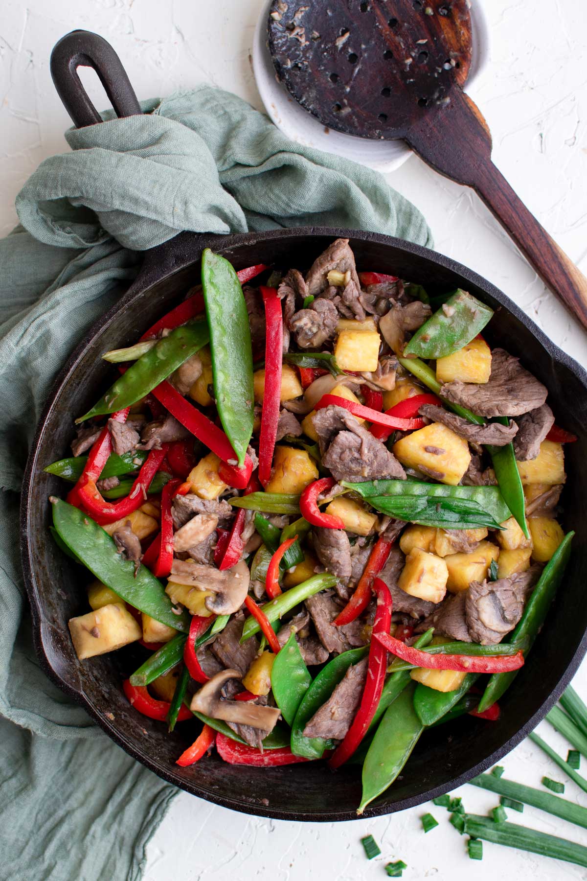 black skillet, green napkin, wood spoon, vegetables and beef in a skillet