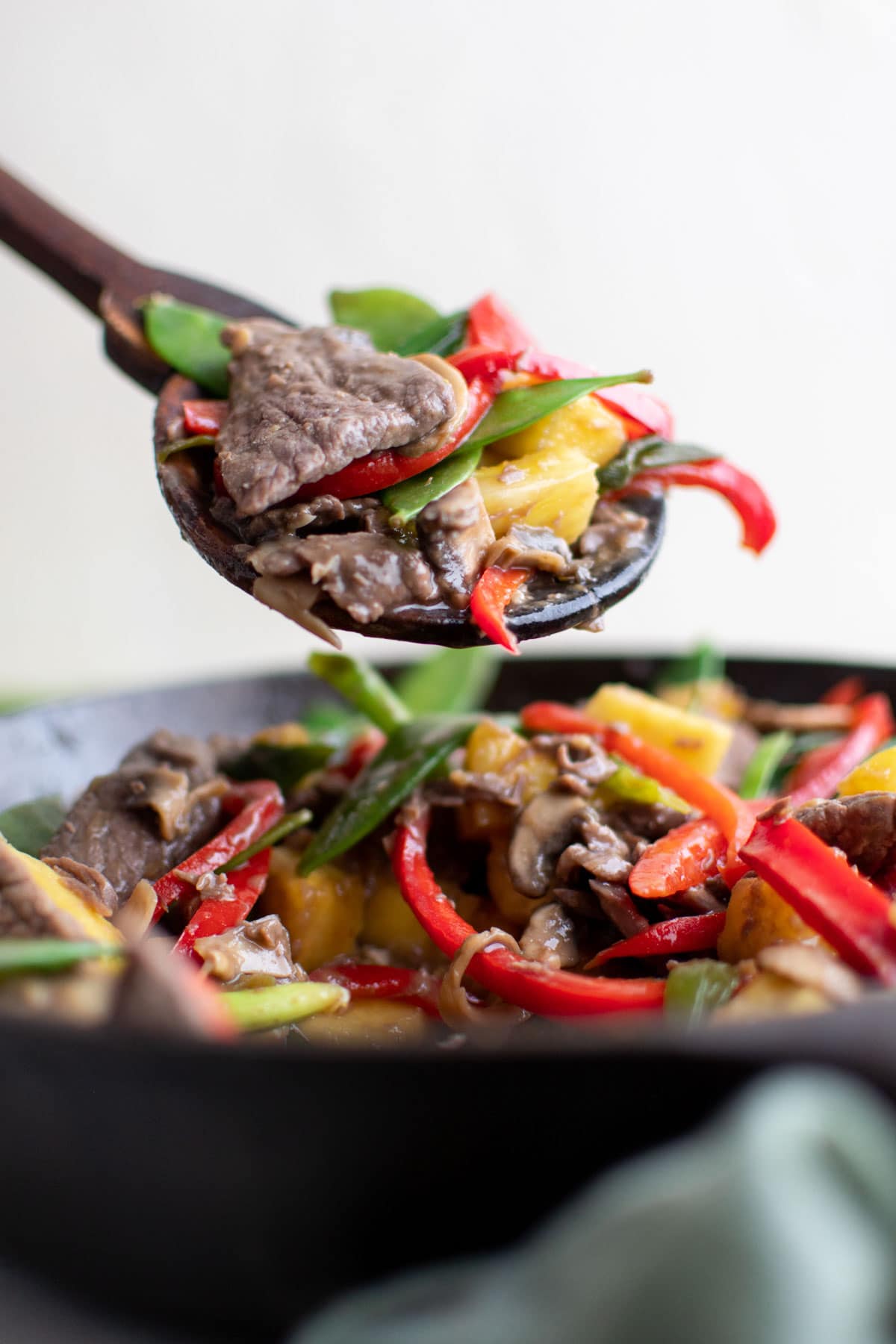 skillet with pineapple beef stir fry, wood spoon