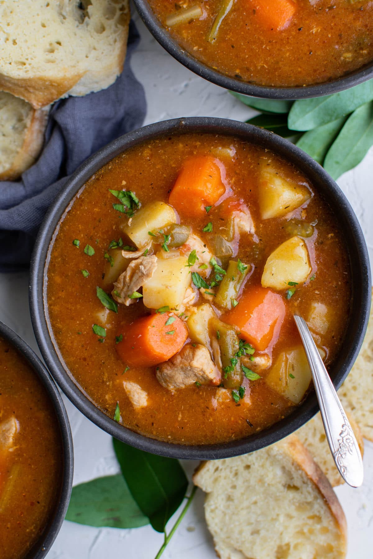 black bowls, potatoes, pork, carrots, blue napkin, bay leaves, bread