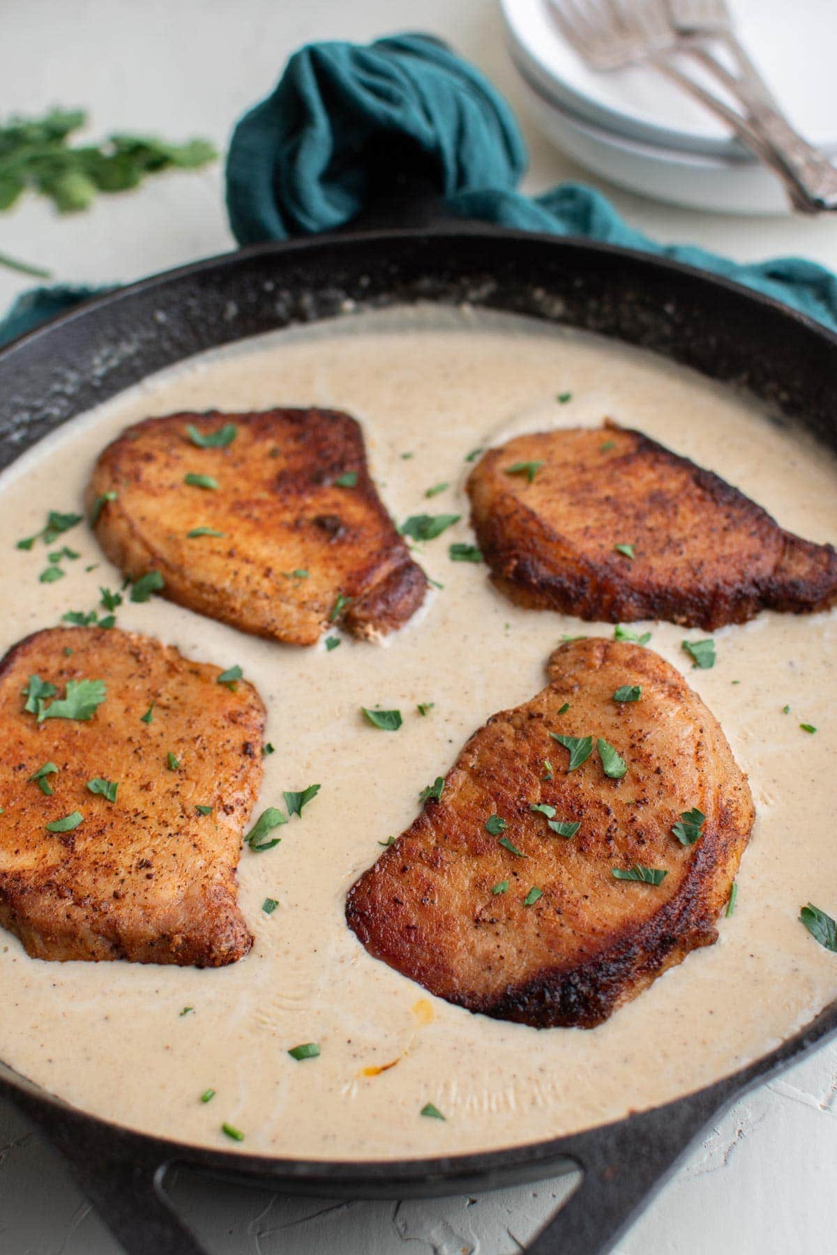 cast iron skillet, gravy pork chops, parsley, blue napkin, white plates, forks