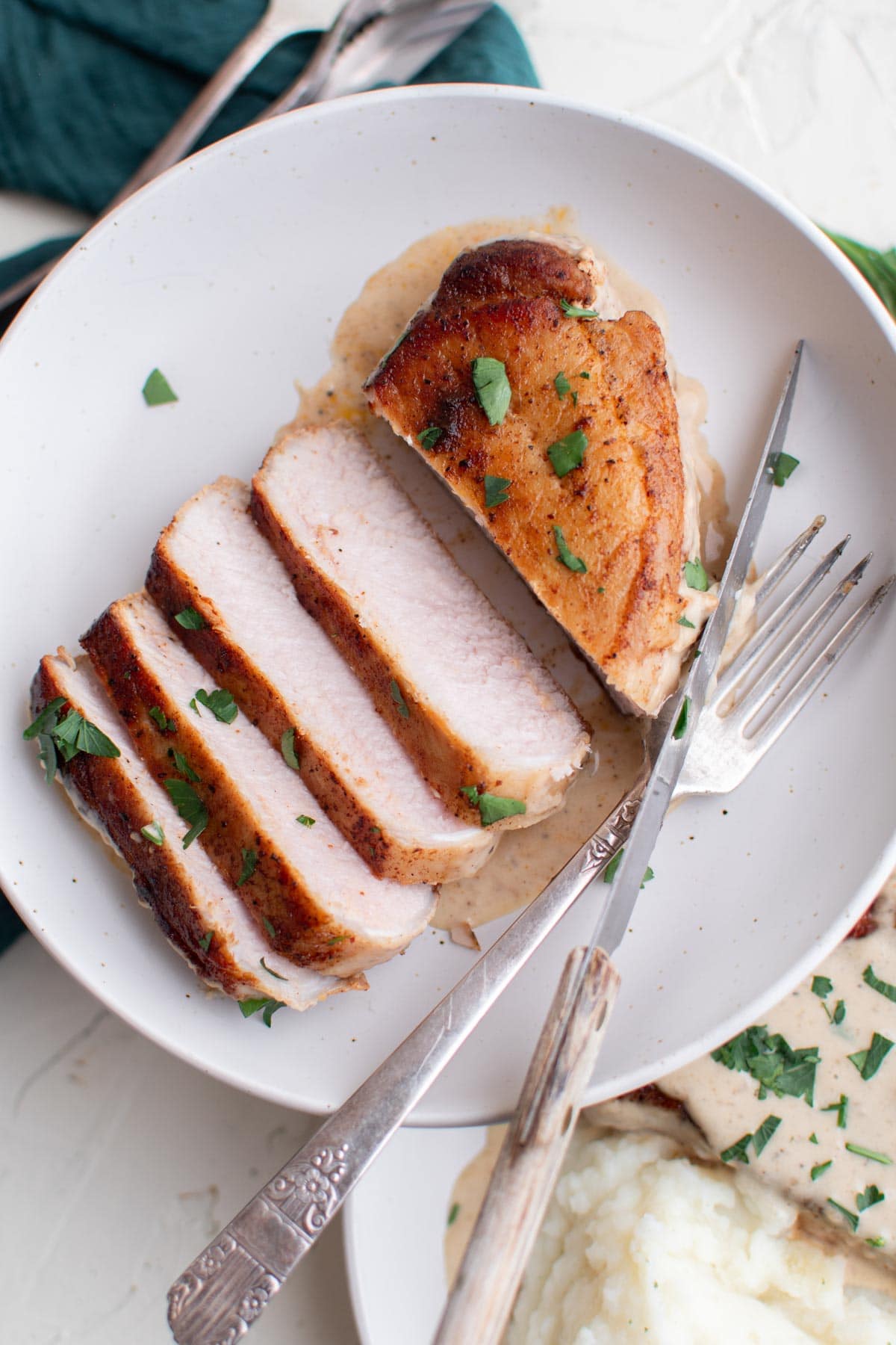 white plate, sliced pork chops, gravy, fork and knife