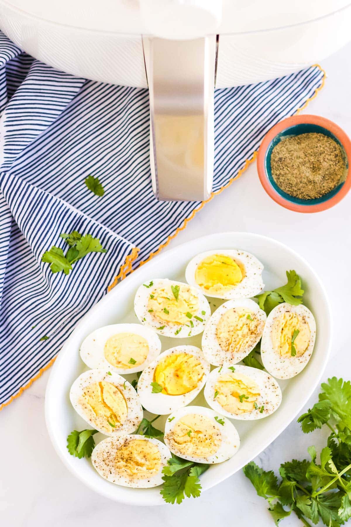 air fryer, white platter of sliced hard boiled eggs, pepper, parsley, blue towel