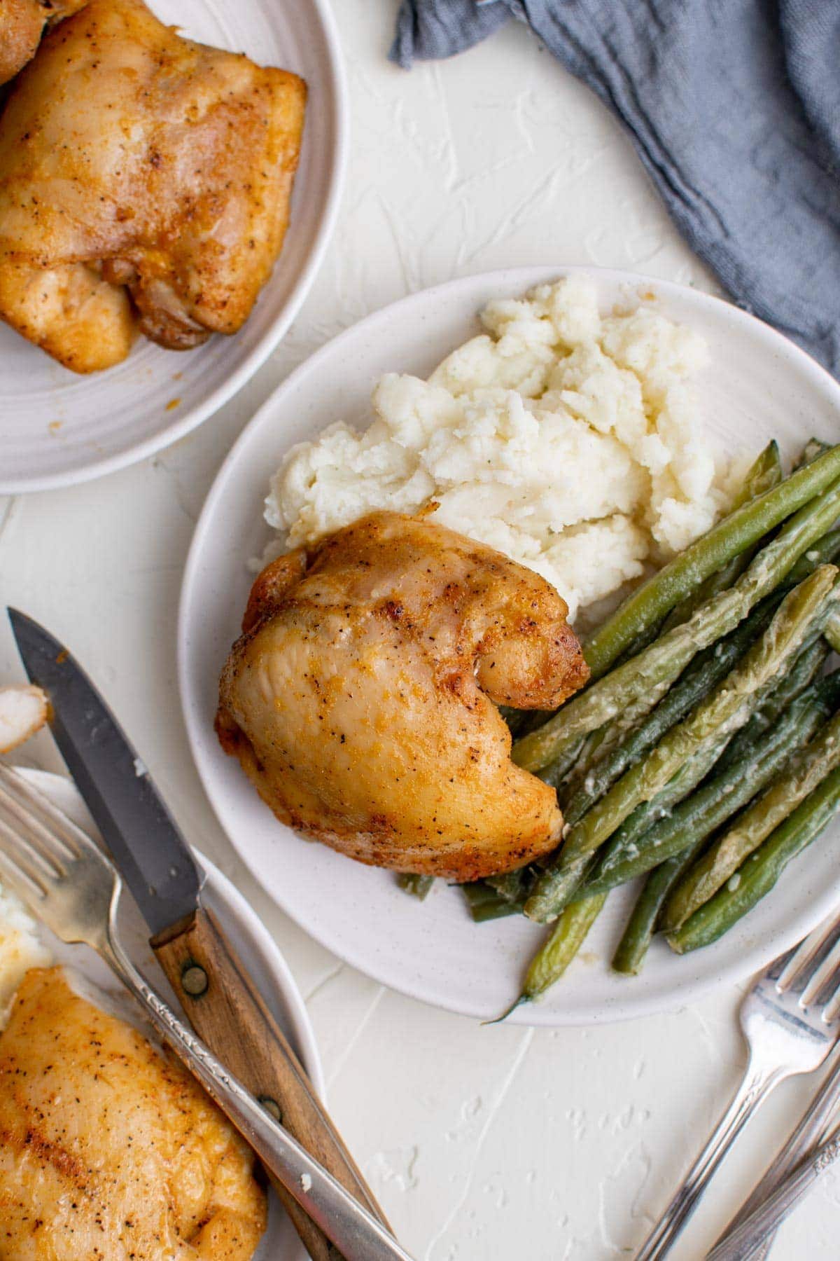 white plates, chicken thighs, green beans, mashed potatoes, forks