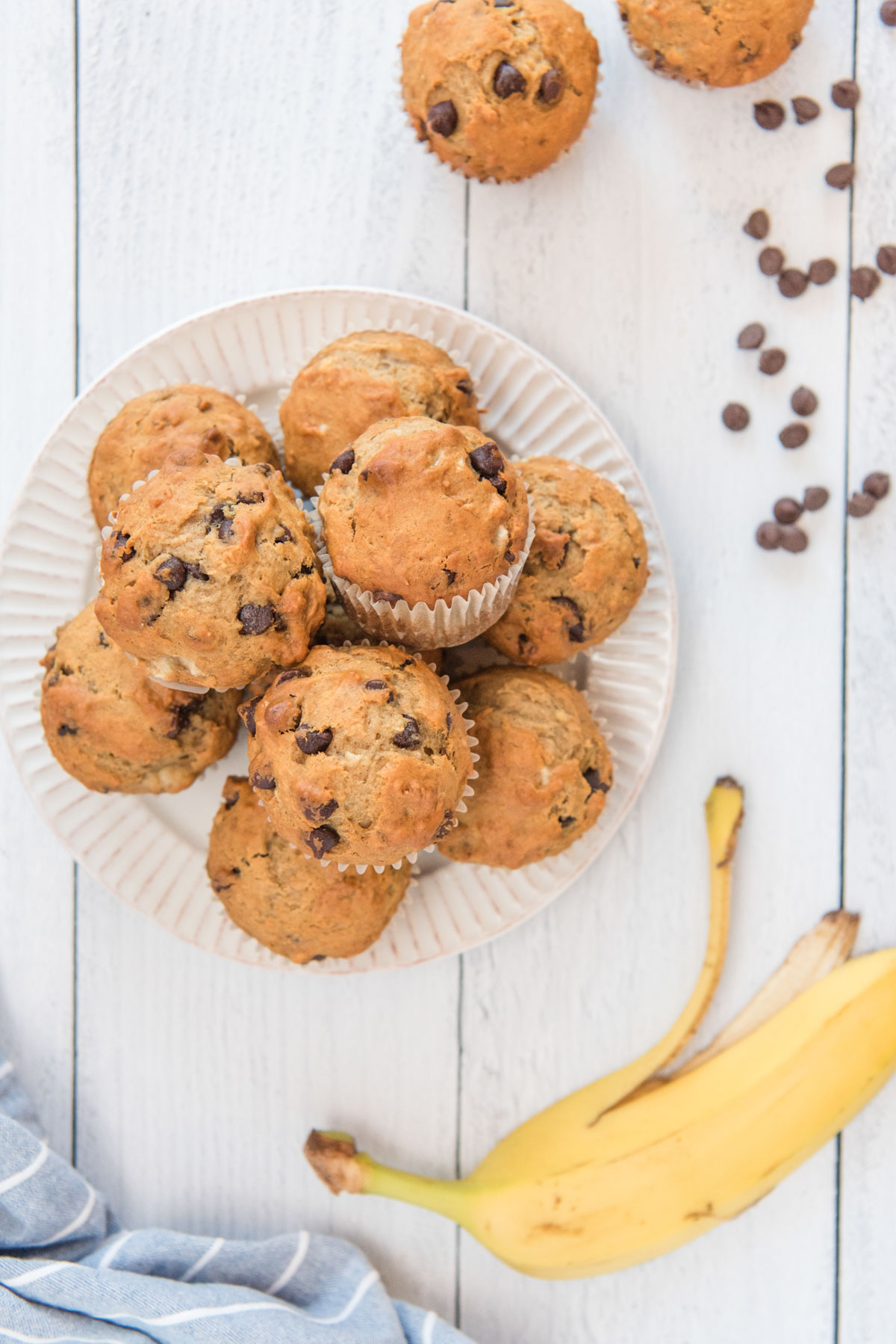 chocolate chips, banana, white plate, chocolate chip banana muffins, white wood background