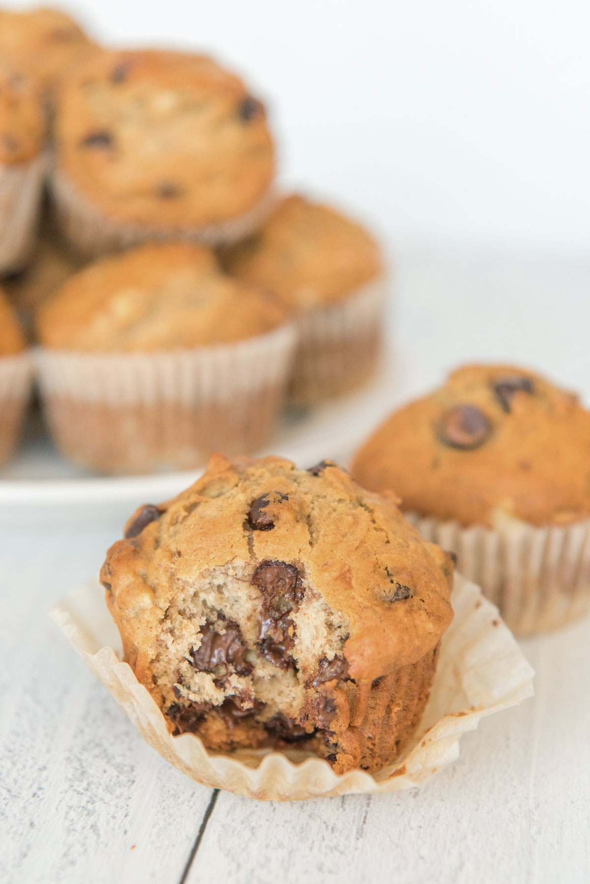 chocolate chip muffin, muffin wrapper, white plate and stack of muffins, 