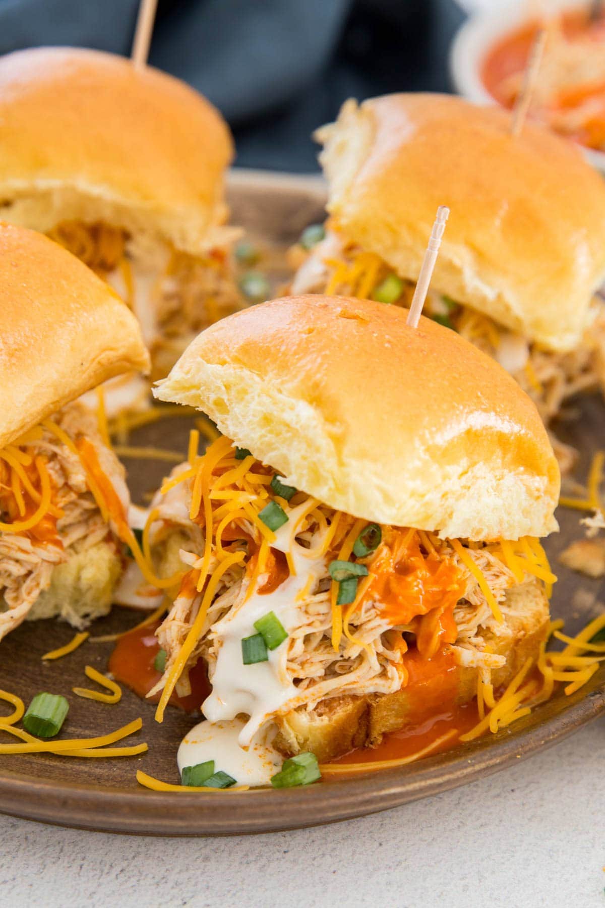 buffalo chicken on slider rolls with green onions, ranch and cheese, toothpicks, gray plate