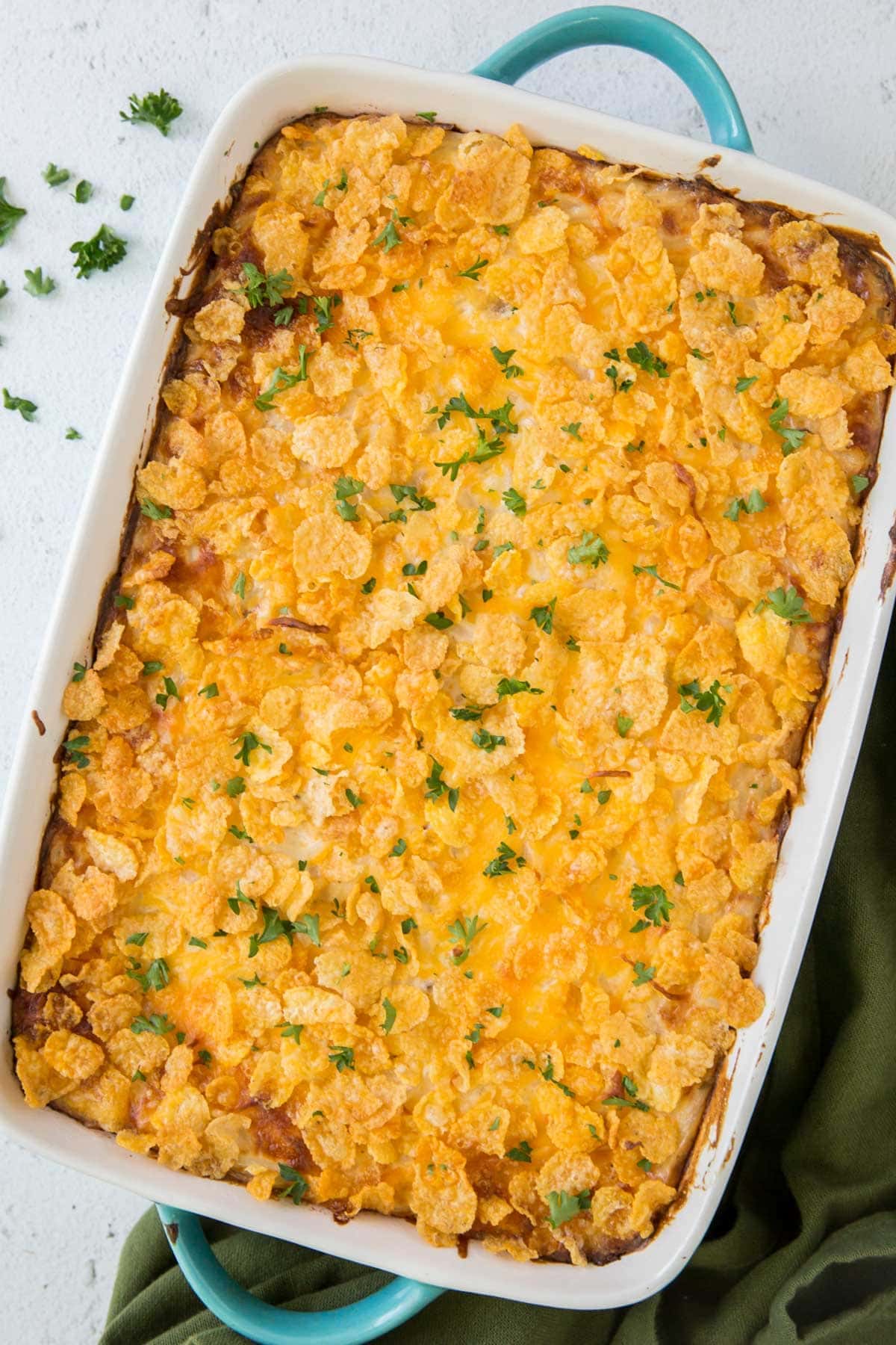 large casserole dish with cornflakes topping over cheesy potatoes, parsley