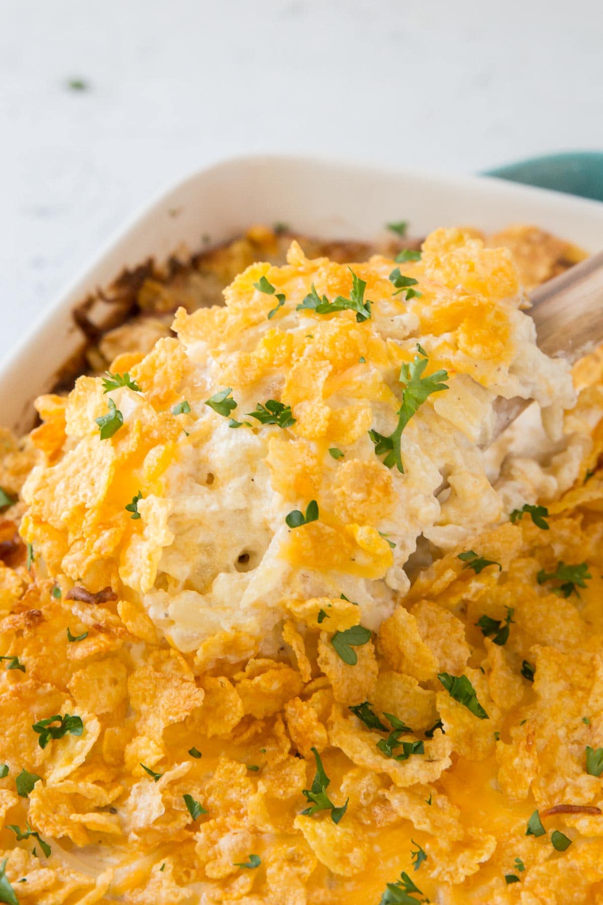 hashbrown casserole with corn flakes topping, wooden spoon, parsley