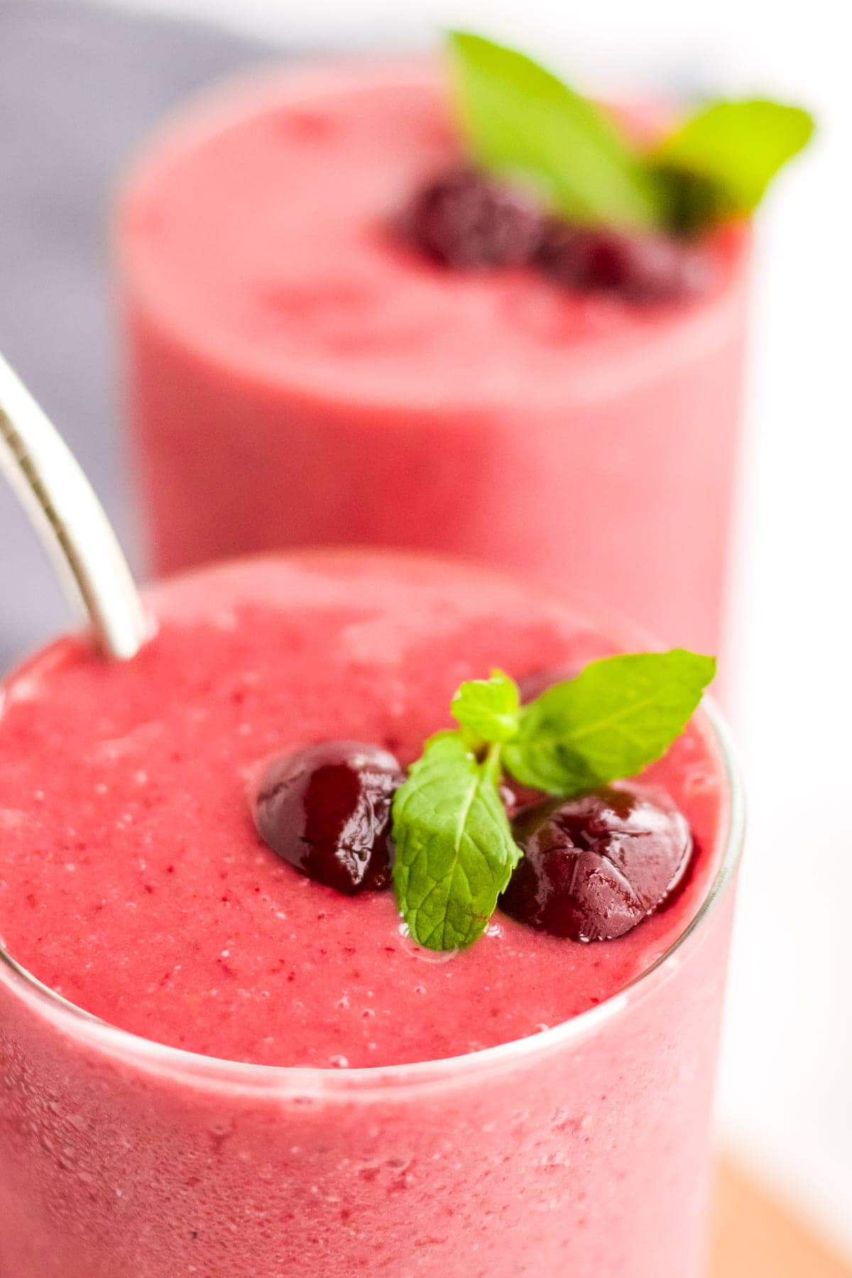 A close up image of a cherry smoothie garnished with cherries and mint. 