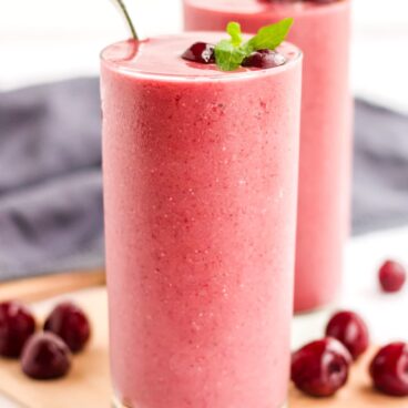 Two glasses of a cherry smoothie recipe garnished with cherries and mint.
