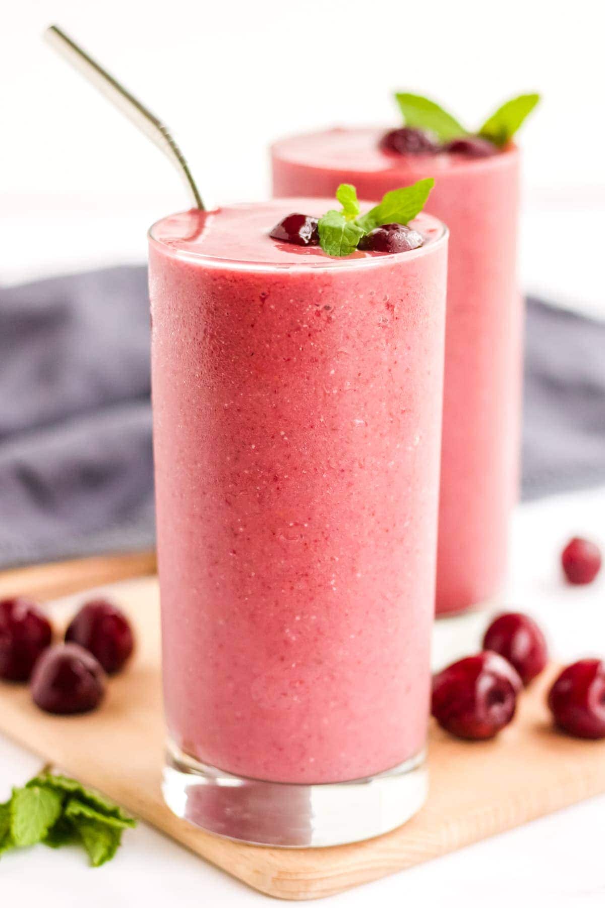 Two glasses of a cherry smoothie recipe garnished with cherries and mint. 