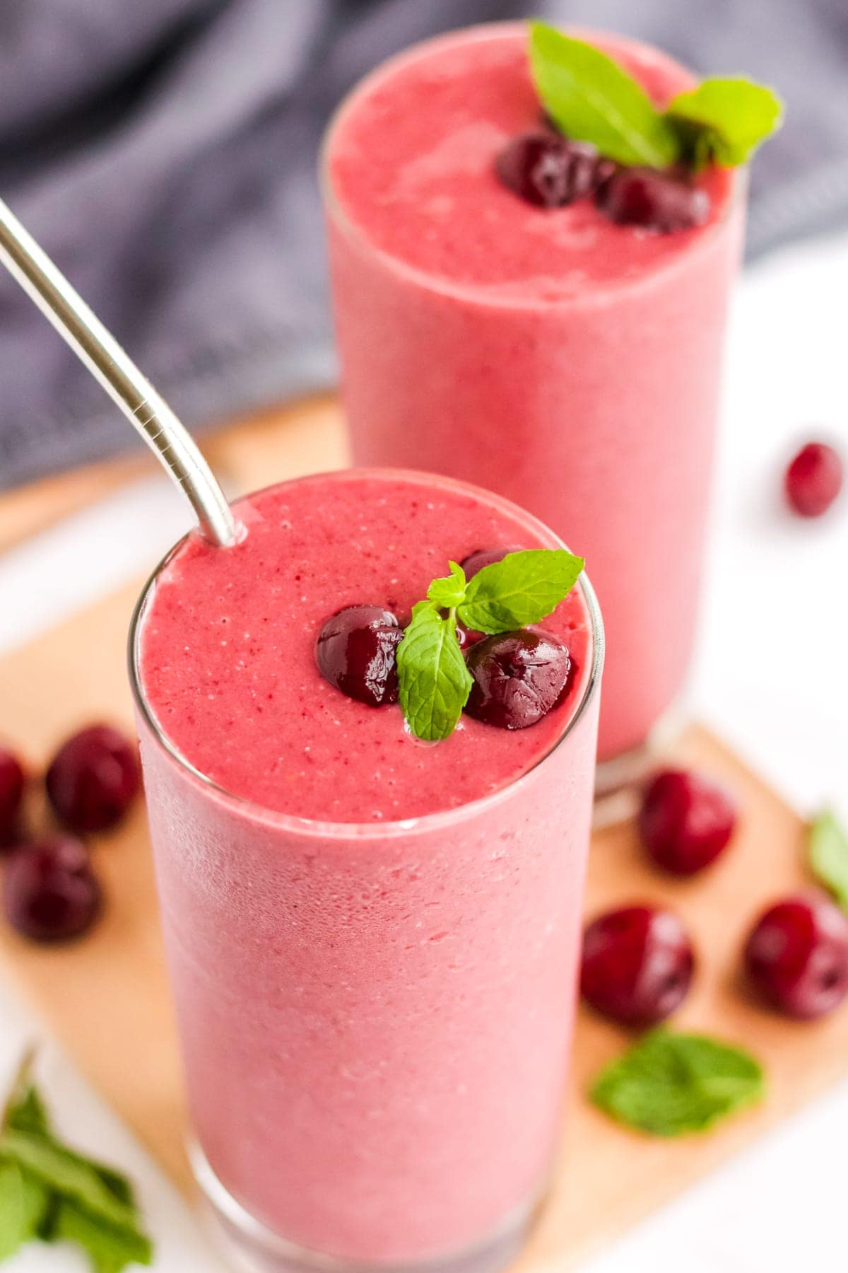 Overhead image of two cherry smoothie recipes with mint leaves and cherries around the glasses. 