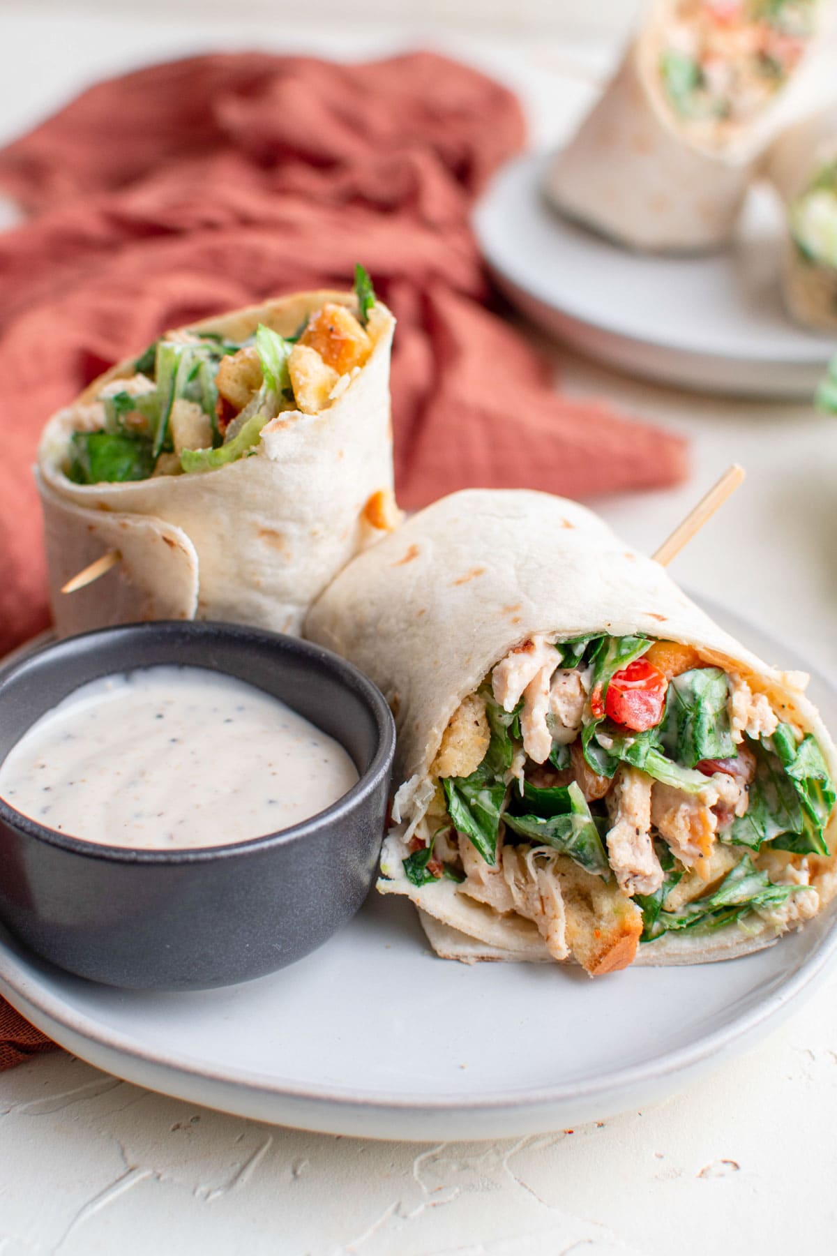 chicken caesar salad wrapped in tortillas, dish of caesar dressing, white plates, pink napkins