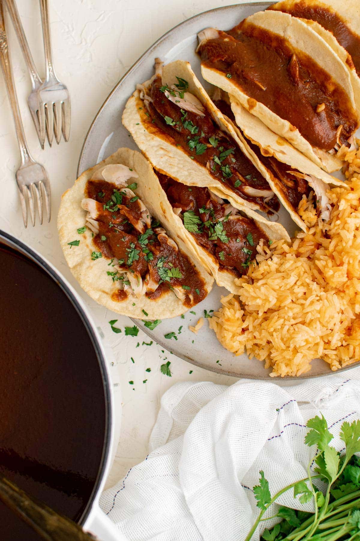 tacos with chicken mole, pan, cilantro, rice, forks, white plate