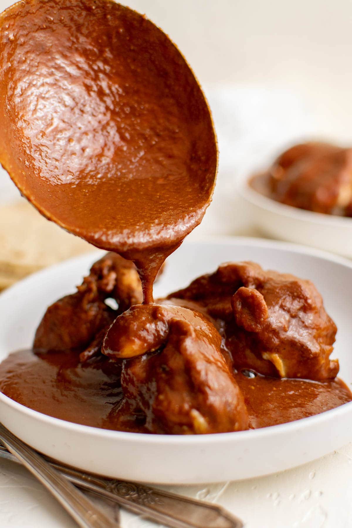 large spoon with mole sauce, chicken in a white plate.