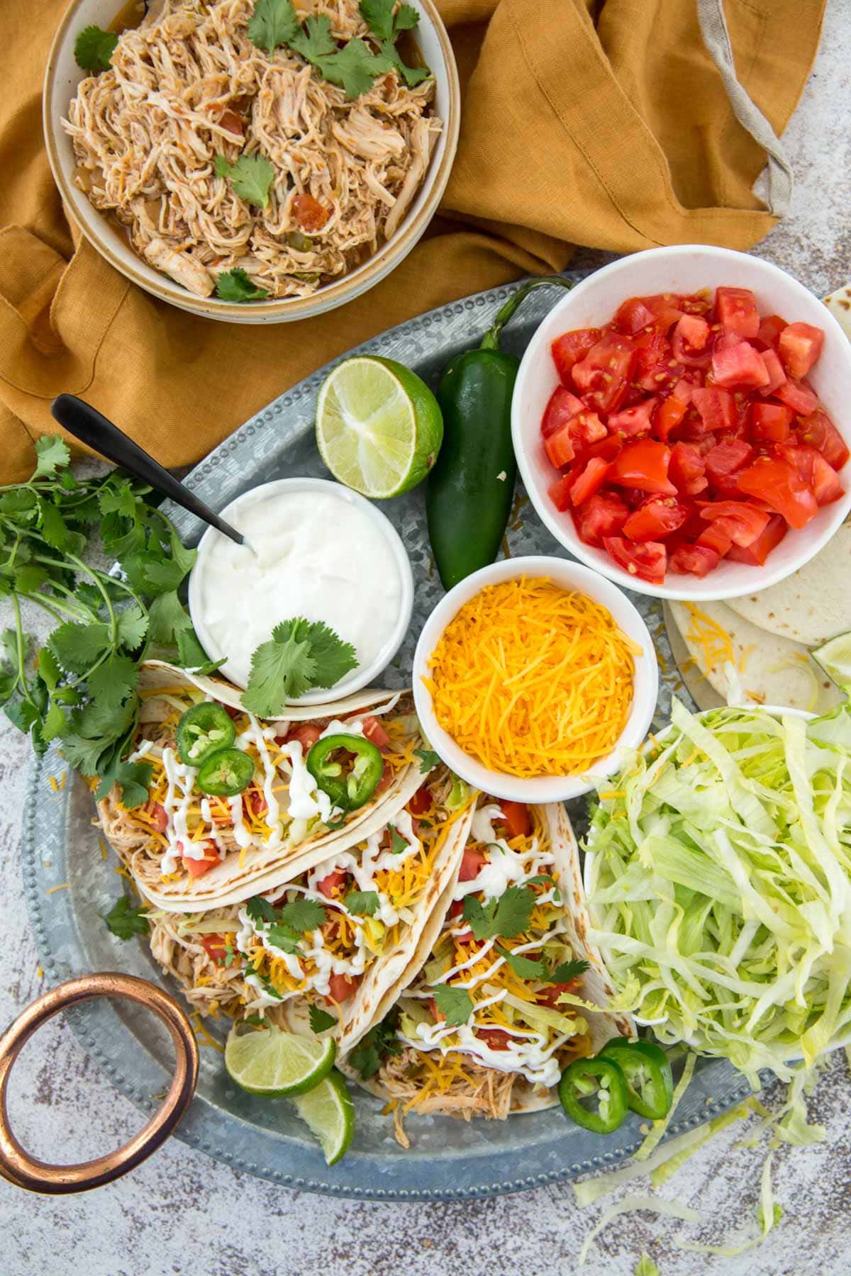 crockpot chicken taco meat in a bowl, tomatoes, sour cream, lettuce, assembled tacos