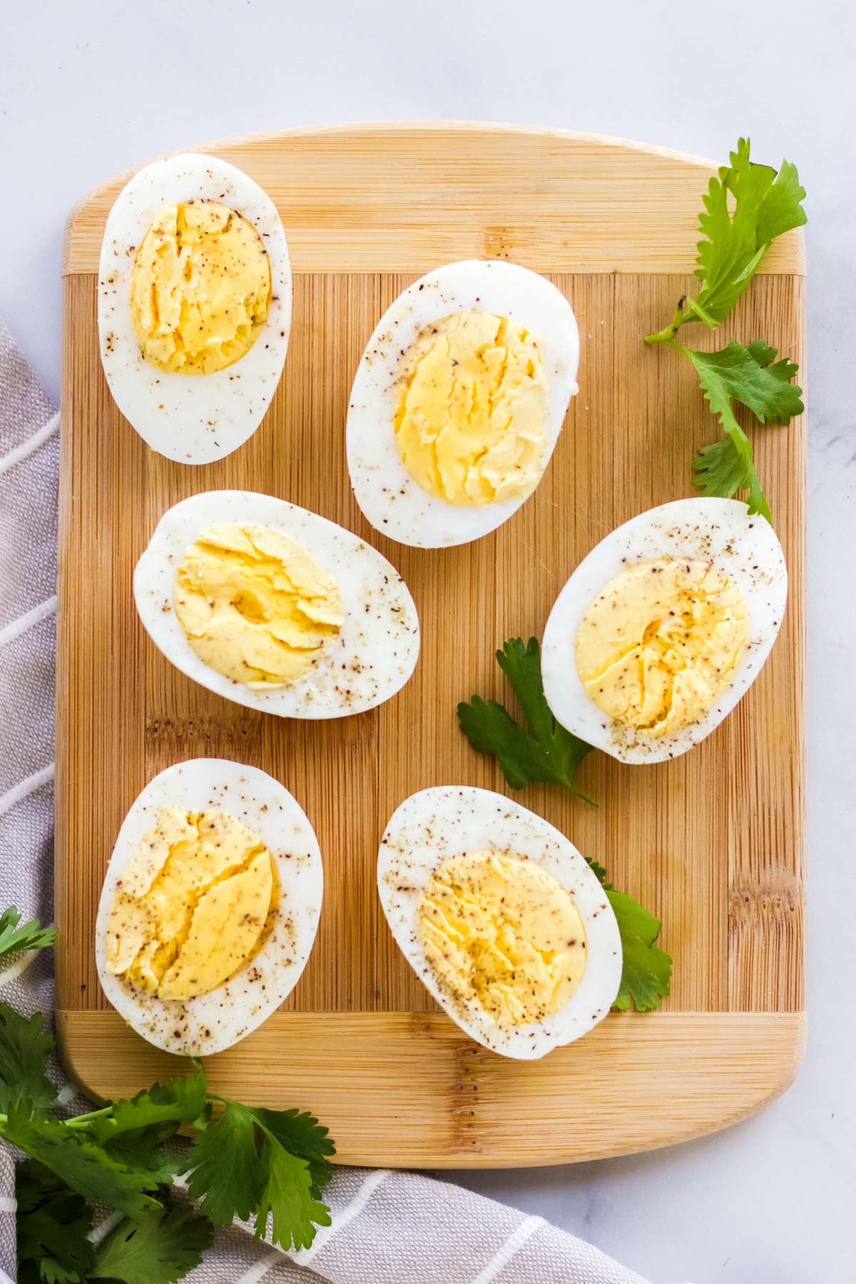 hard boiled eggs, sliced in half, wood cutting board, parsley, gray striped towel, pepper