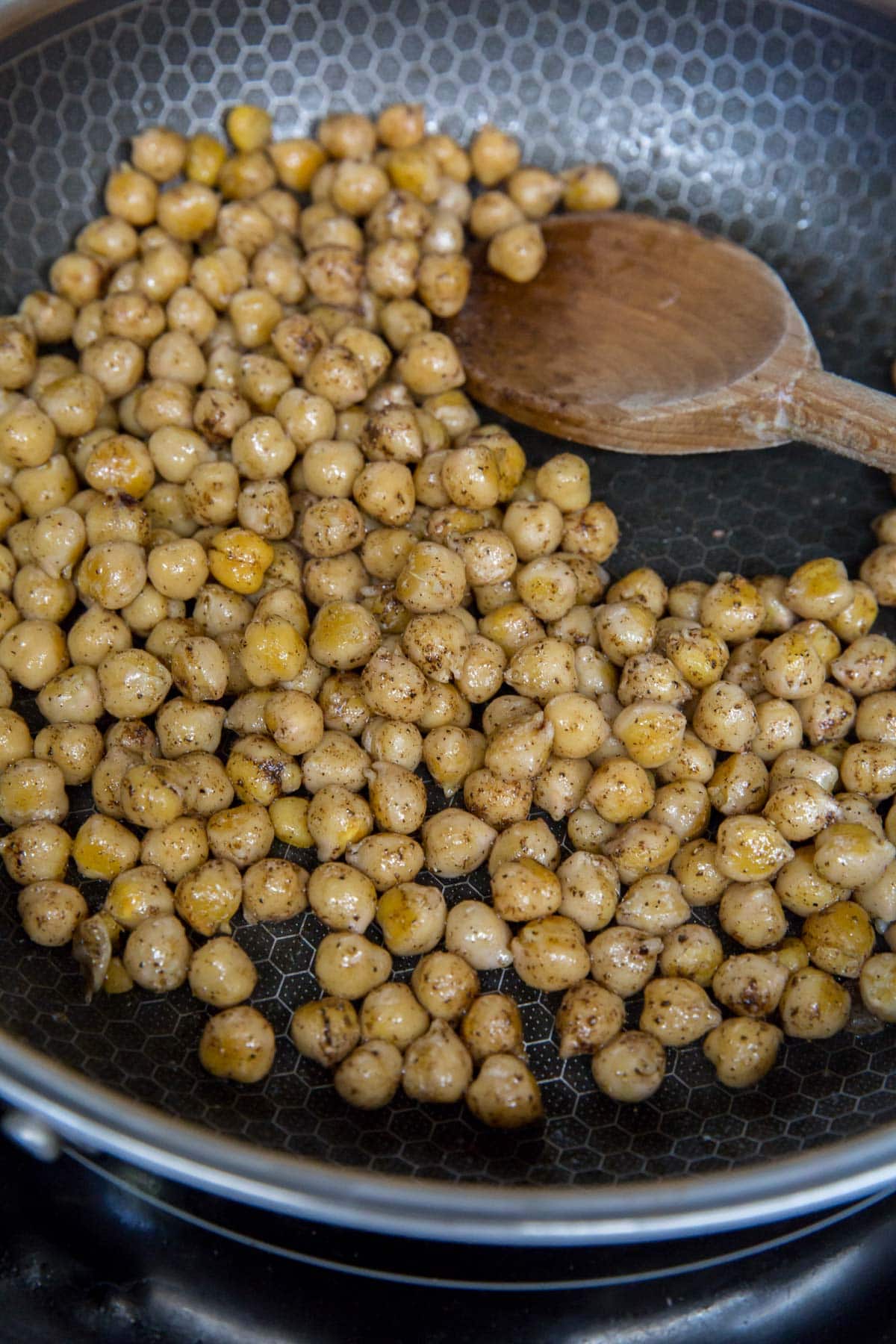 chickpeas toasting in a skillet with a wooden spoon