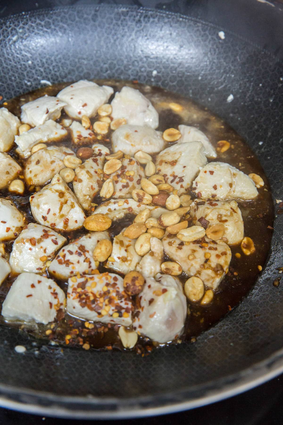 black wok, chicken pieces, peanuts, red pepper flakes, sauce