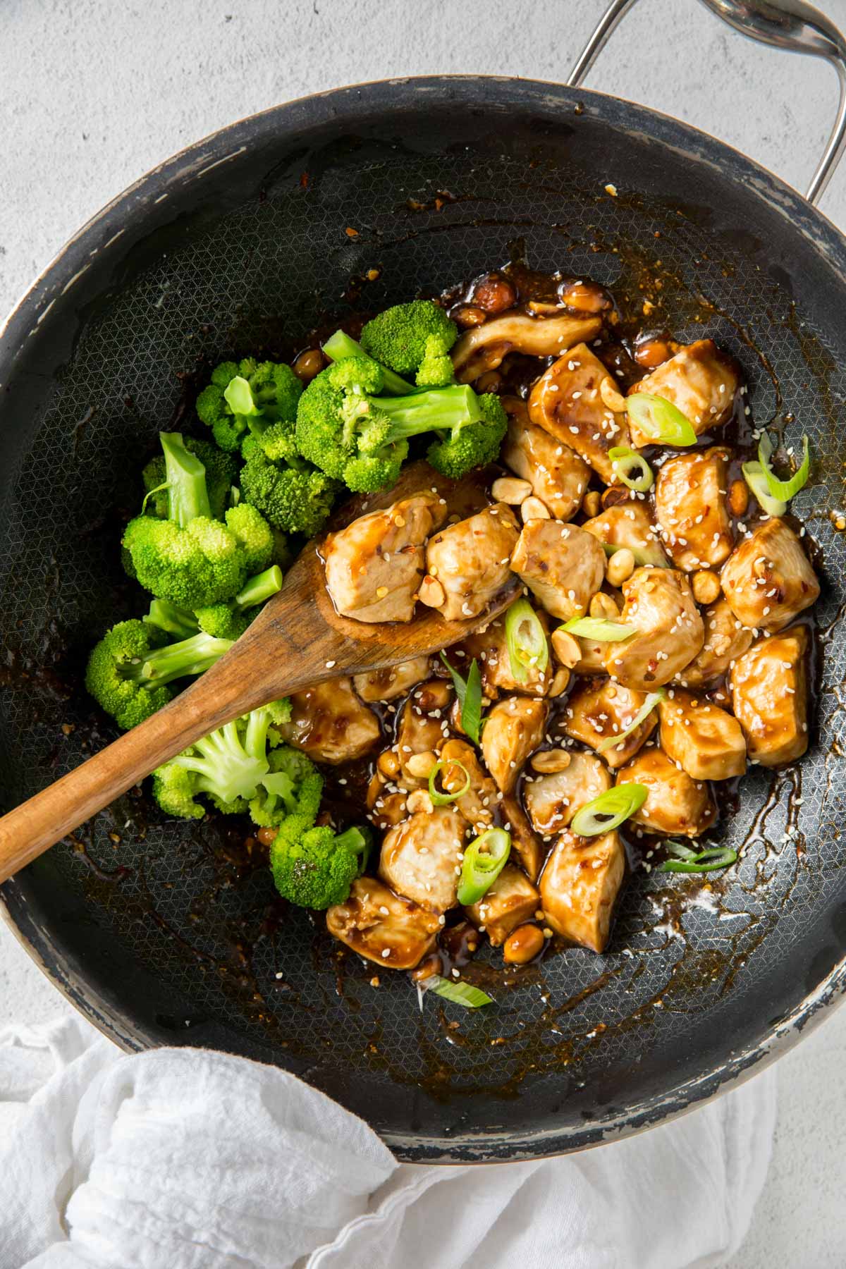 black wok, kung pao chicken, broccoli, wooden spoon, green onions, peanuts