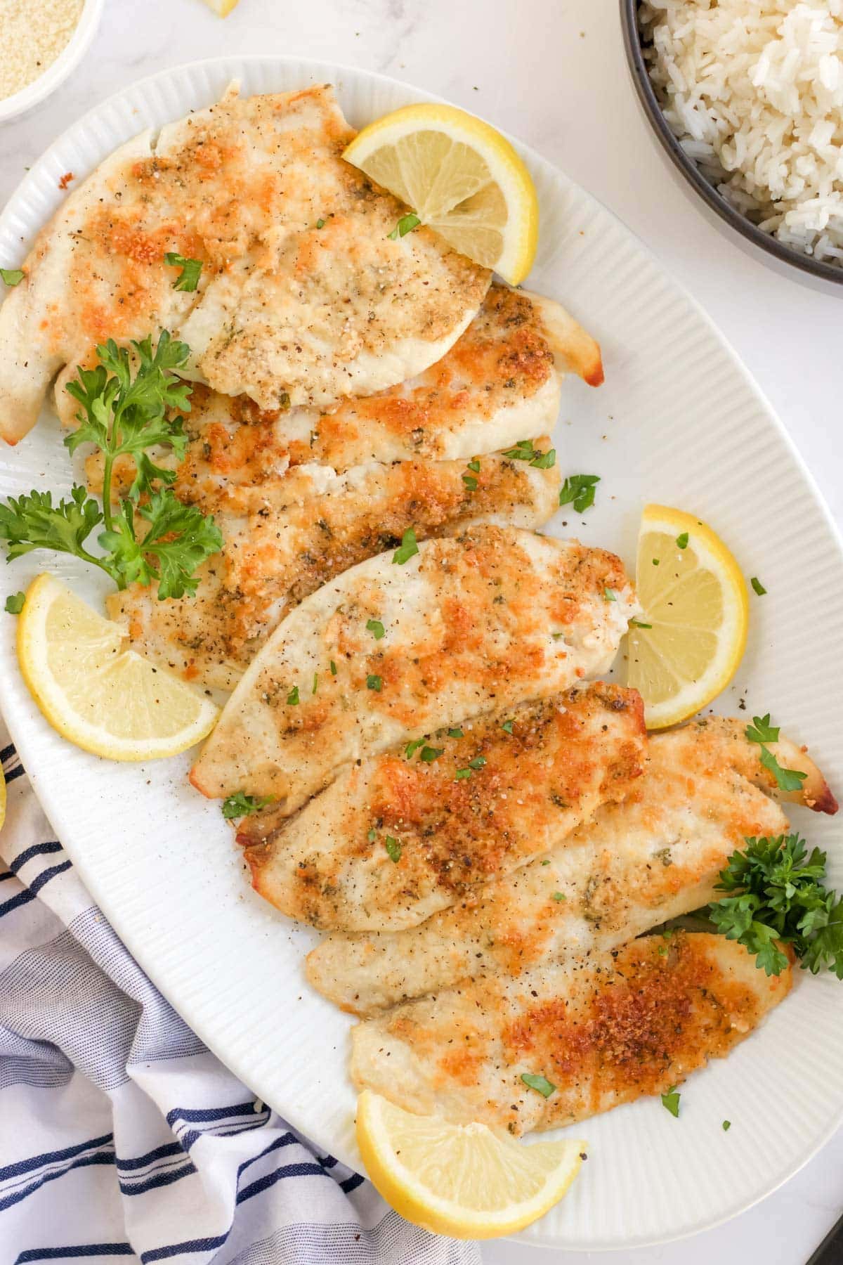 white platter of parmesan crusted tilapia, lemon slices, parsley