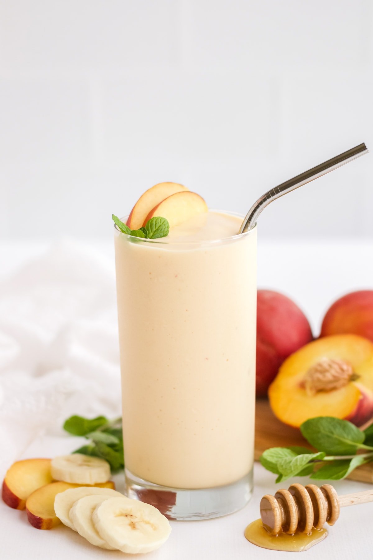 Peach Smoothie on a white styling board with ingredients laid out around the glass. 