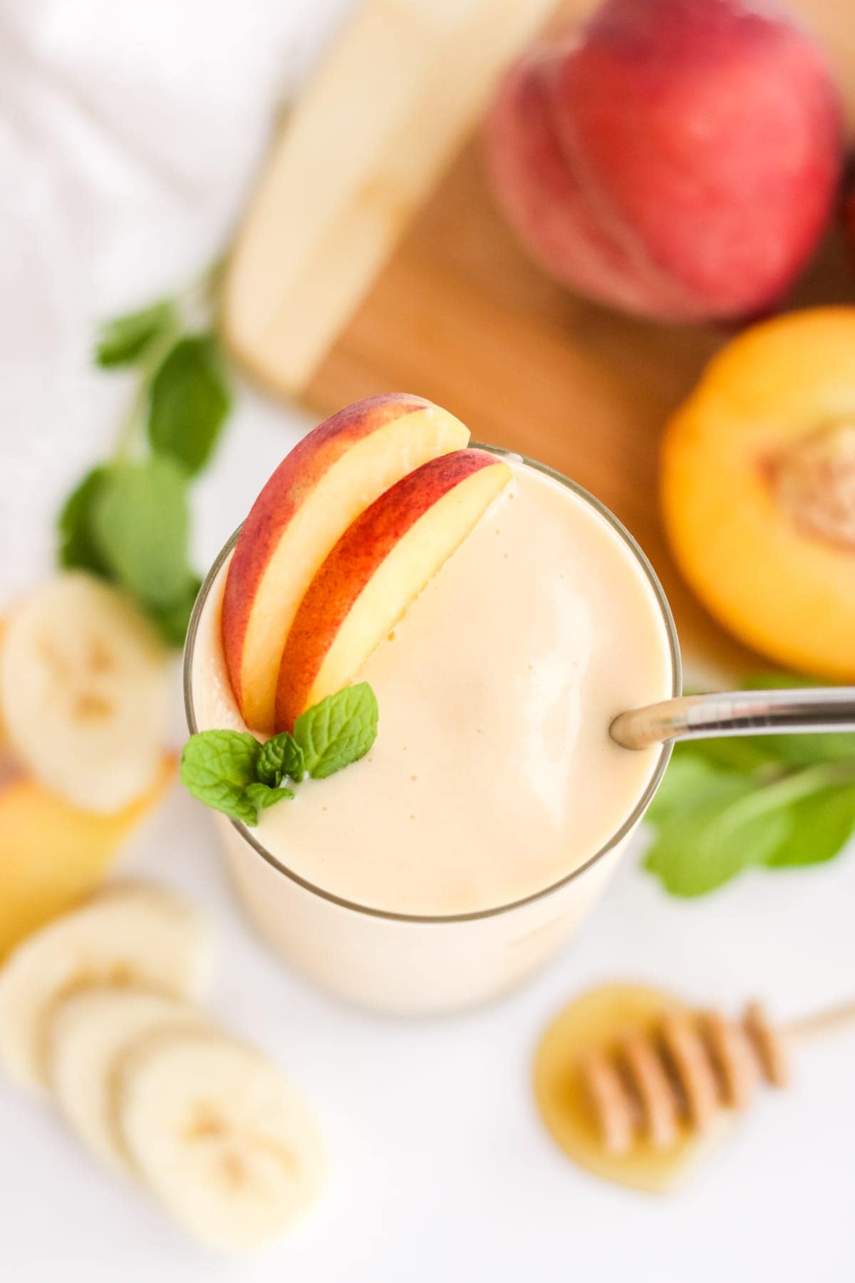 An overhead image of a peach banana smoothie with a slice of peach and mint on the top.