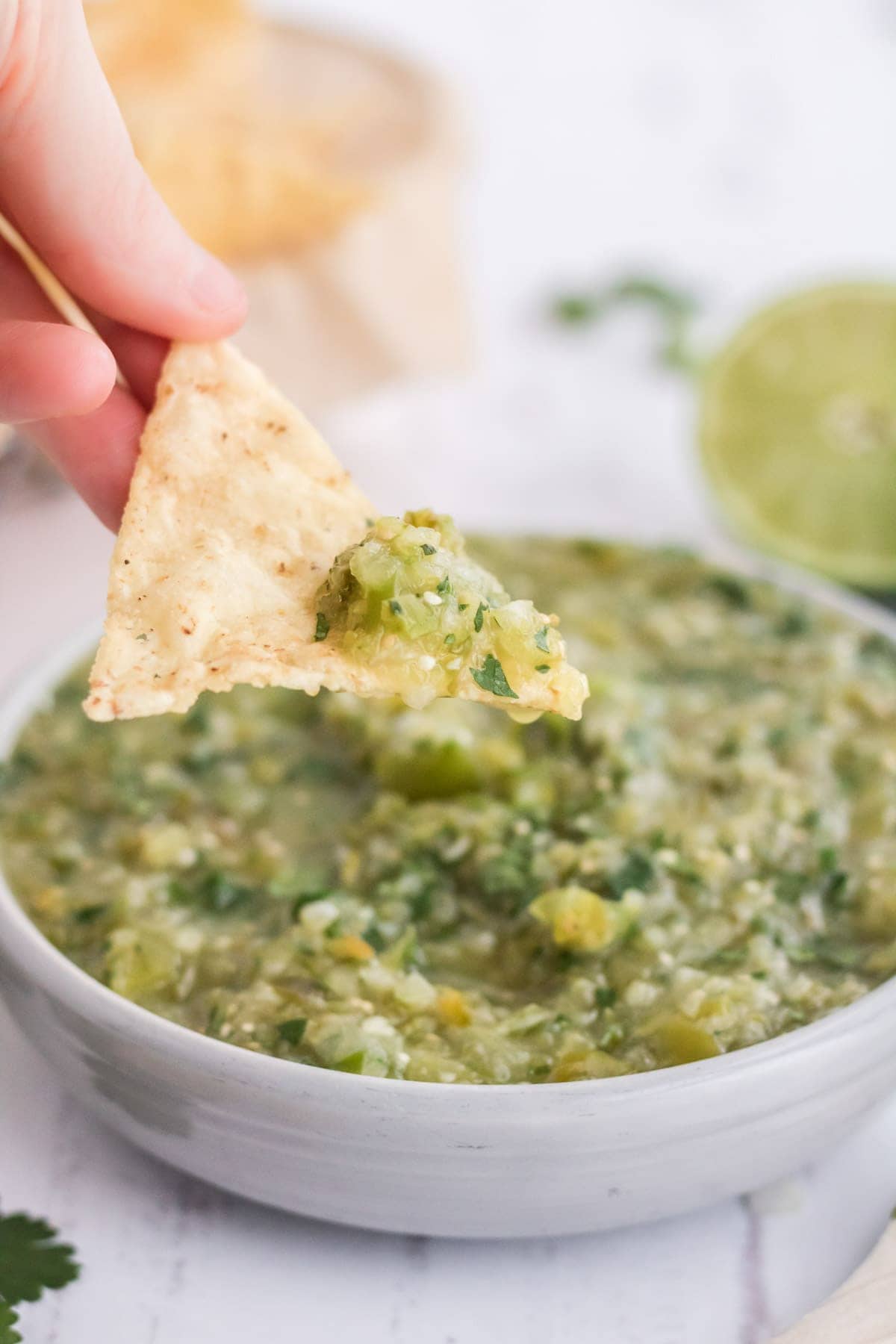 chip dipping in salsa verde, limes, white bowl