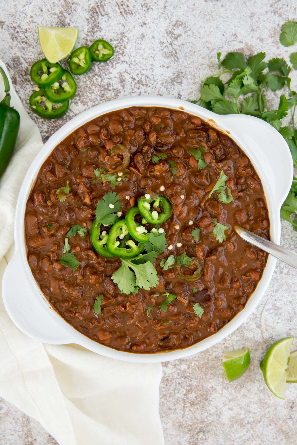 white bowl mexican beans, jalapenos, cilantro, limes, spoon