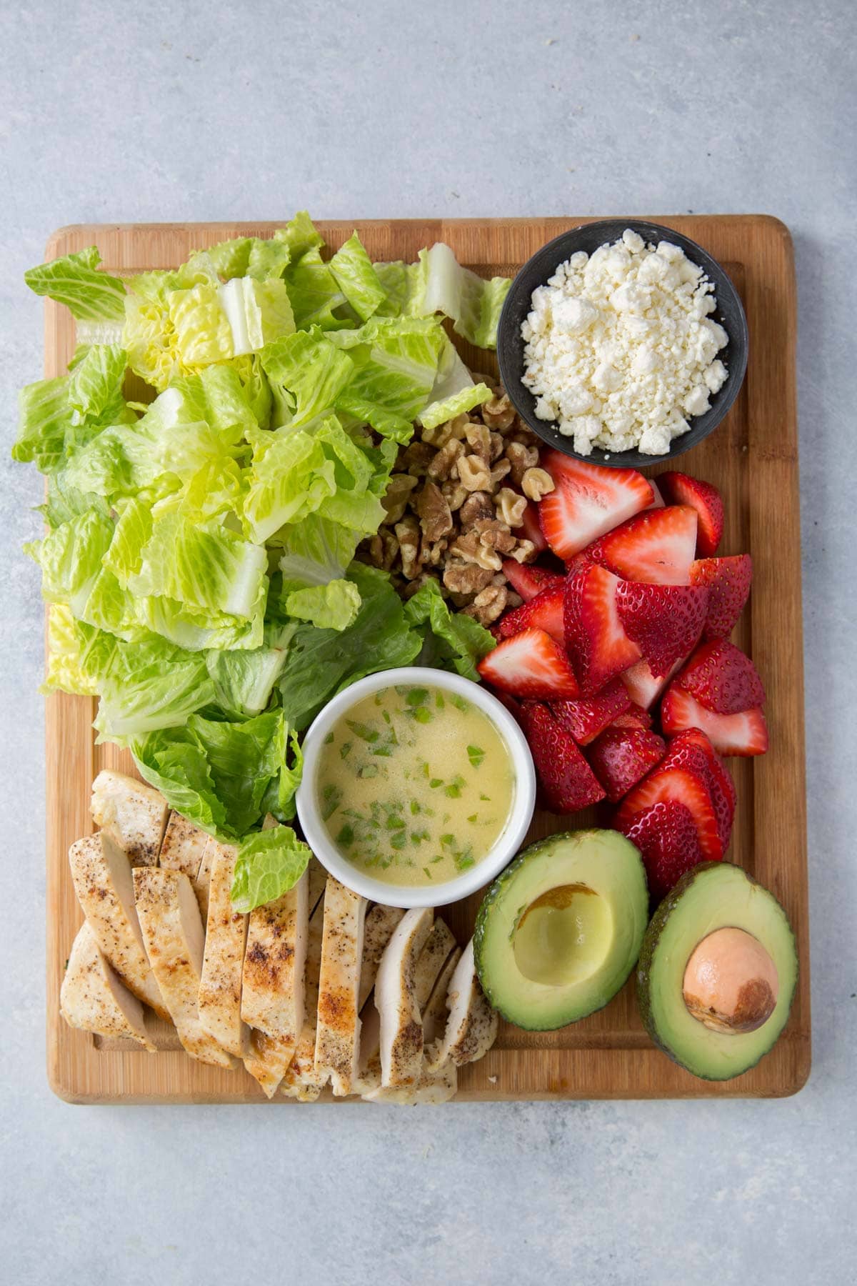 lettuce, feta, avocado, vinaigrette chicken, strawberries, walnut, on a wood cutting board