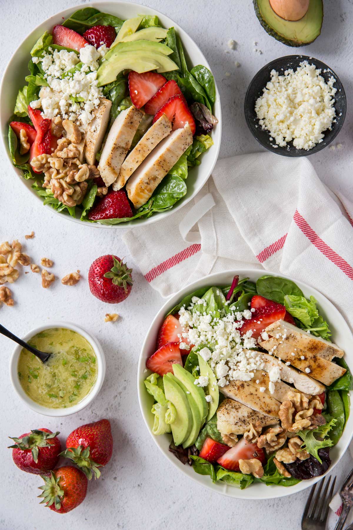 two white bowls with salad, chicken, strawberries, avocado, feta, dressing, forks